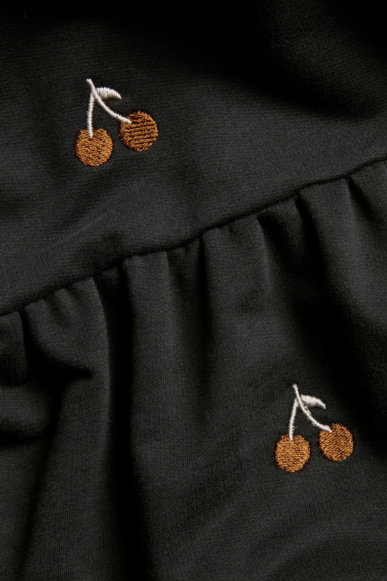 Zbliżenie czarnej bawełnianej sukienki dresowej z brązowym haftem wiśni i marszczonym szwem.