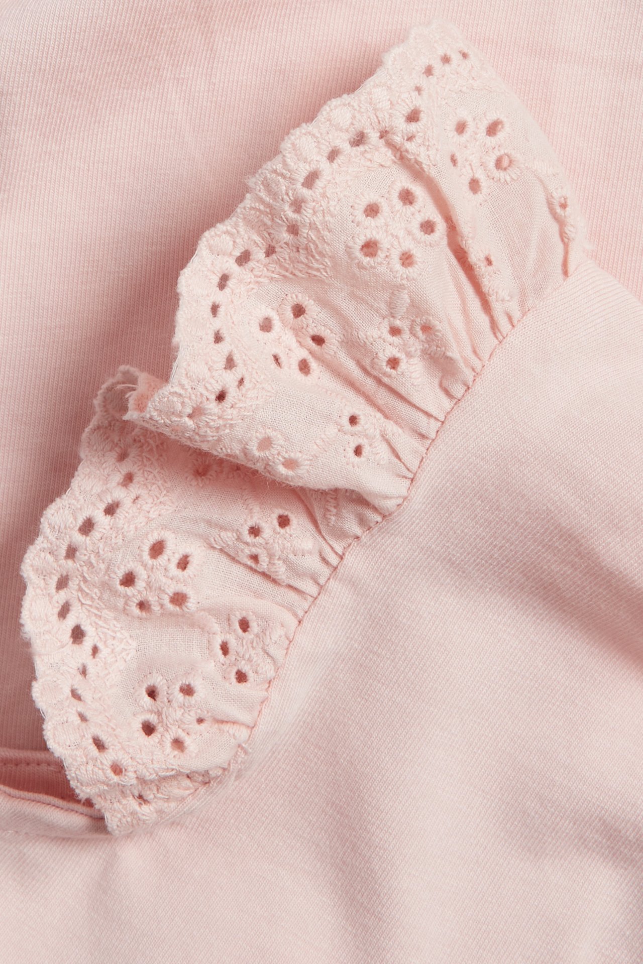Nærbilde av en lys rosa babybody med volangerm i bomullsblonde.
