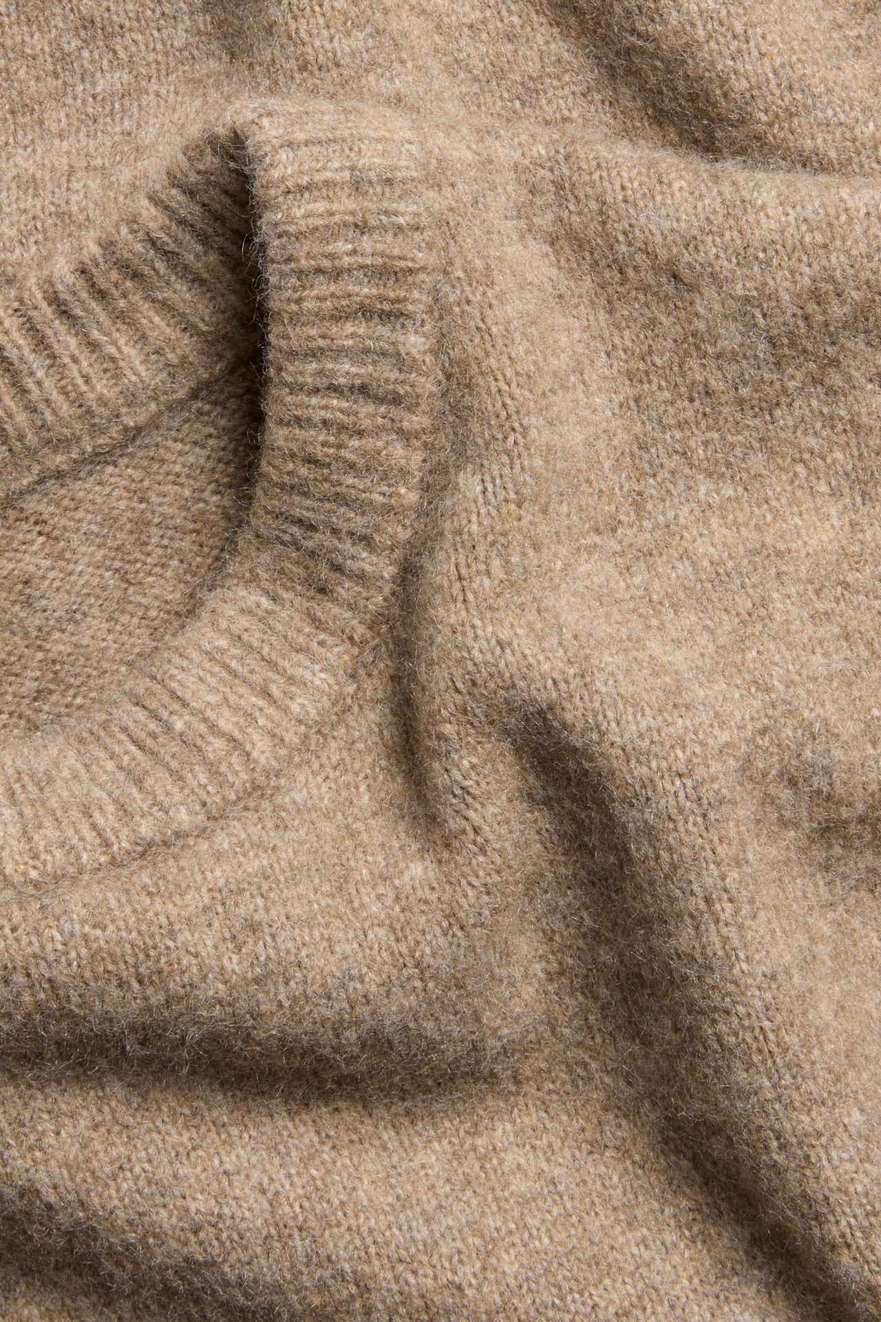 Zbliżenie beżowego melanżowego swetra z drobnej dzianiny z prążkowanym dekoltem.