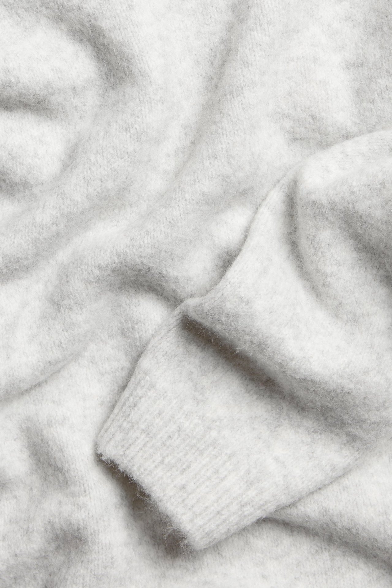 Zbliżenie miękkiego, jasnoszarego melanżowego swetra z delikatnej dzianiny ze ściągaczem.