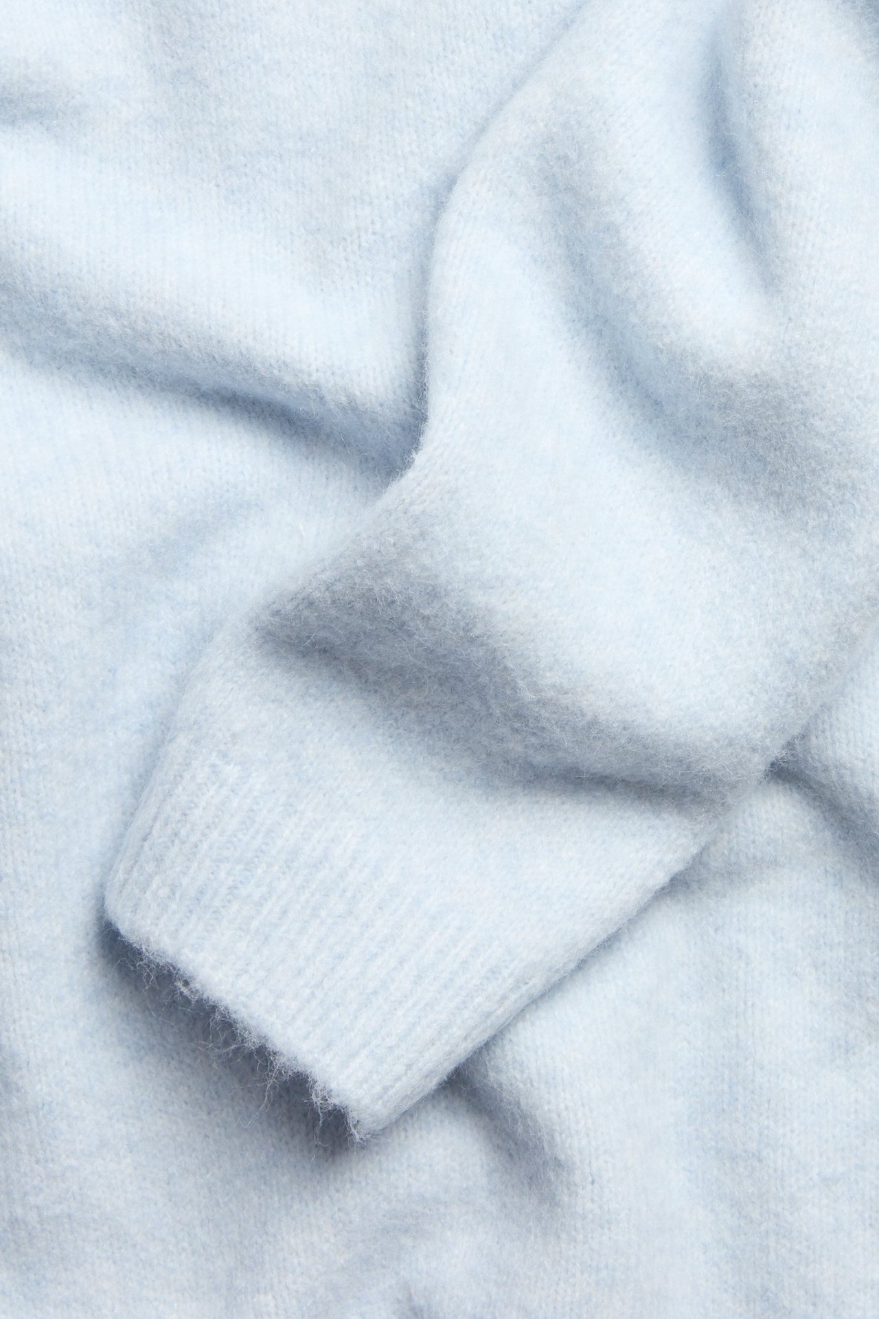 Zbliżenie jasnoniebieskiego, miękkiego, drobno dzianego swetra ze ściągaczem.