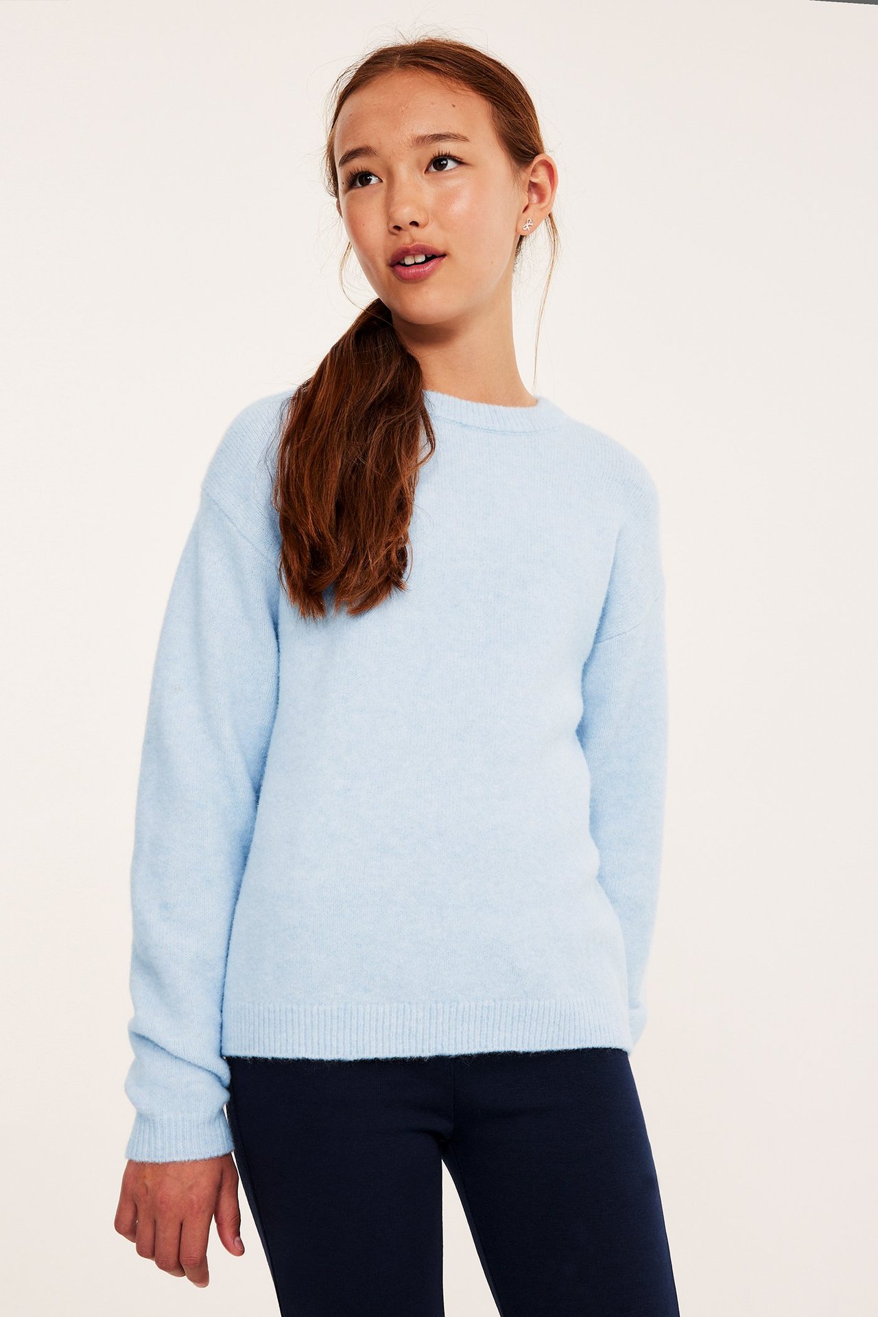 Widok z przodu: dziecko w jasnoniebieskim swetrze z cienkiej dzianiny i granatowych spodniach.