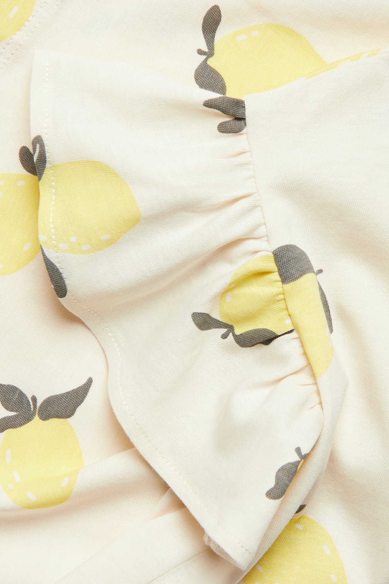 Närbild av offwhite bomullstopp med gult citronprint och volangärm.