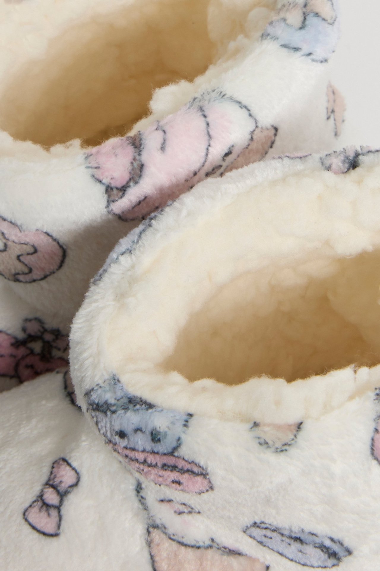 Lähikuva luonnonvalkoisista pörröisistä tohveleista, joissa on värikäs keksikuvio ja kermanvärinen vuori.