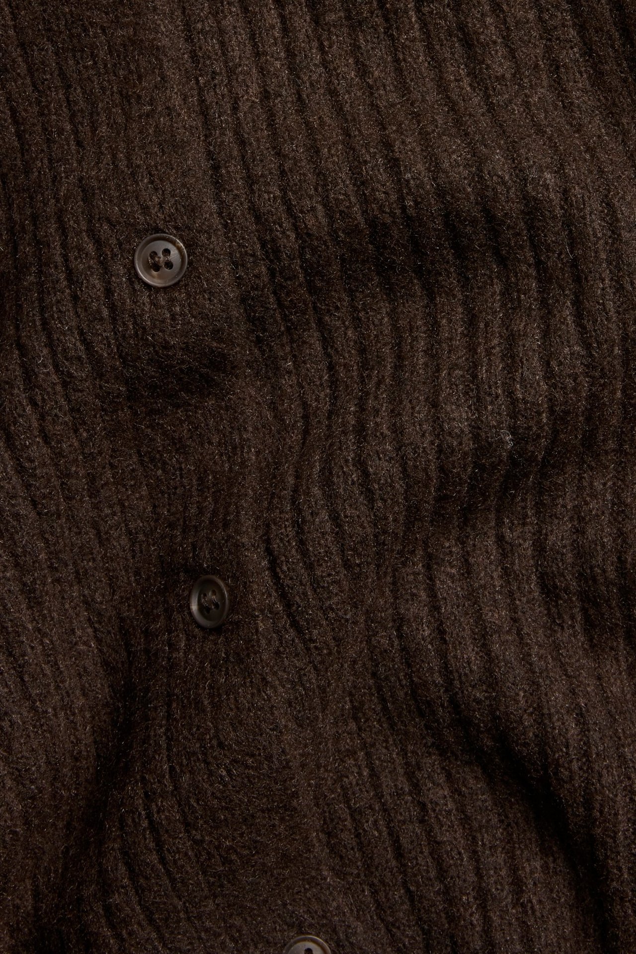Zbliżenie brązowego, prążkowanego, dzianinowego, krótkiego kardiganu z widocznymi guzikami.