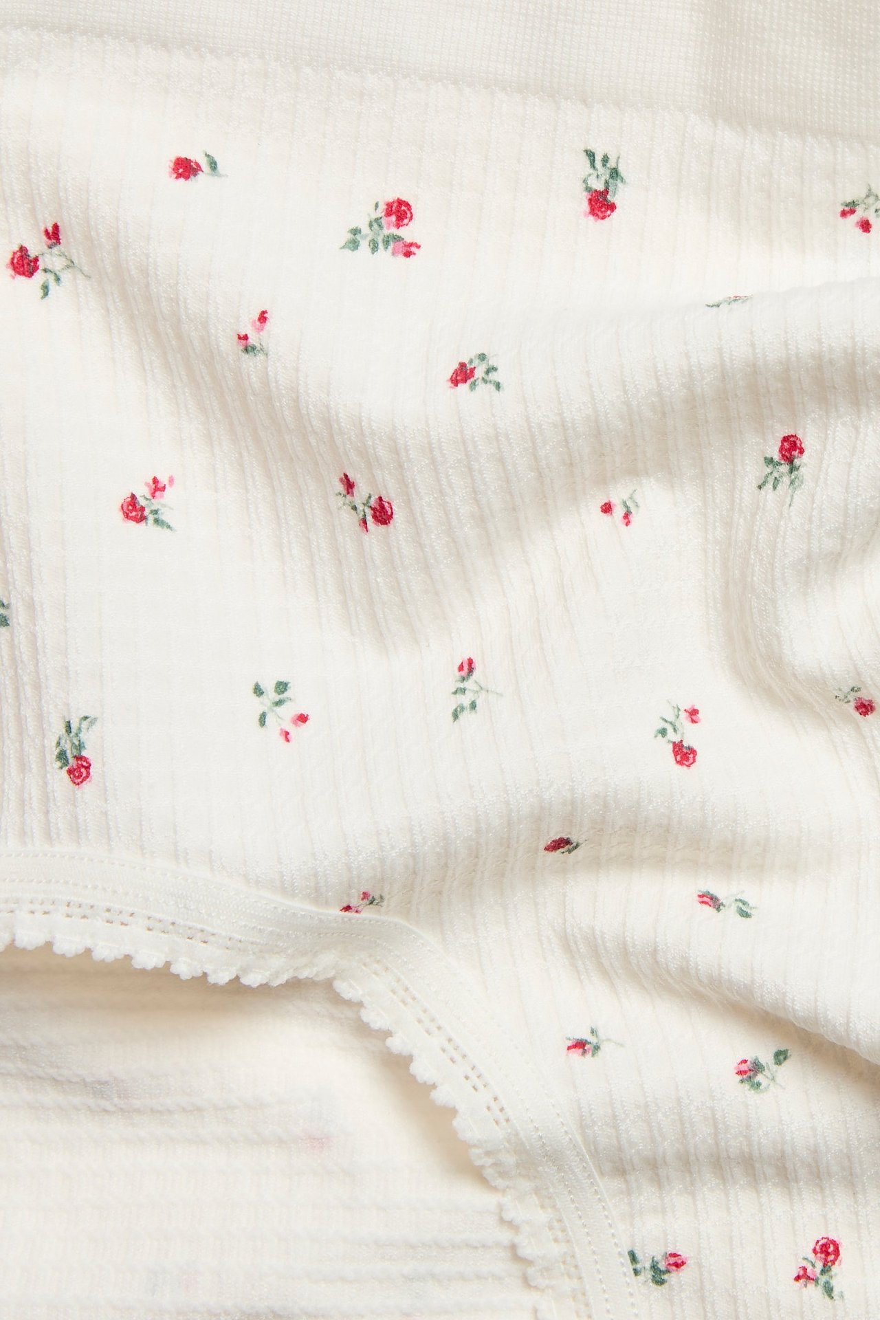 Zbliżenie białych, bezszwowych, prążkowanych fig typu hipster z małym wzorem w czerwone róże i koronką.