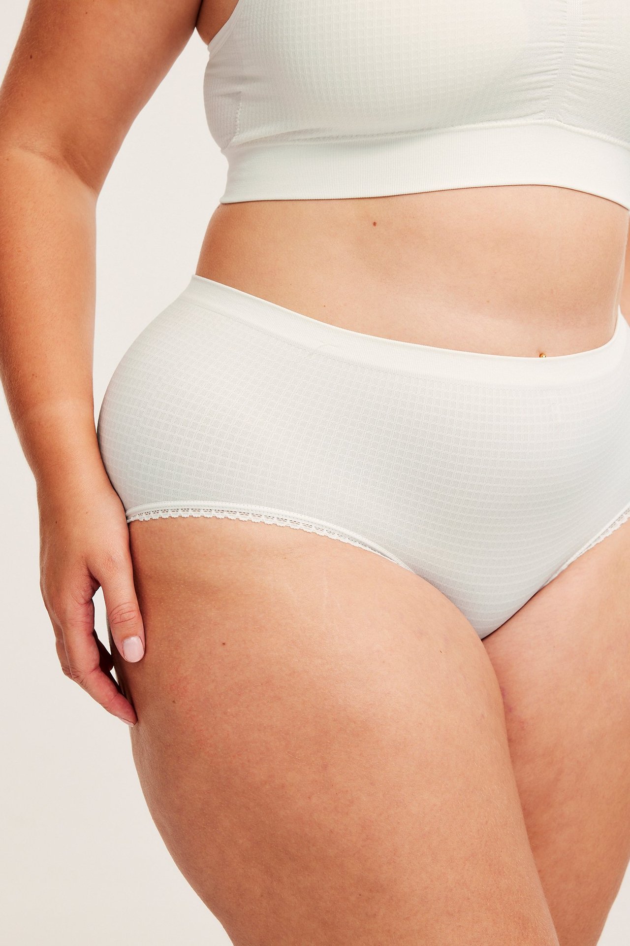 Närbild på kvinna i vita sömlösa strukturerade hipstertrosor med spets och matchande BH.