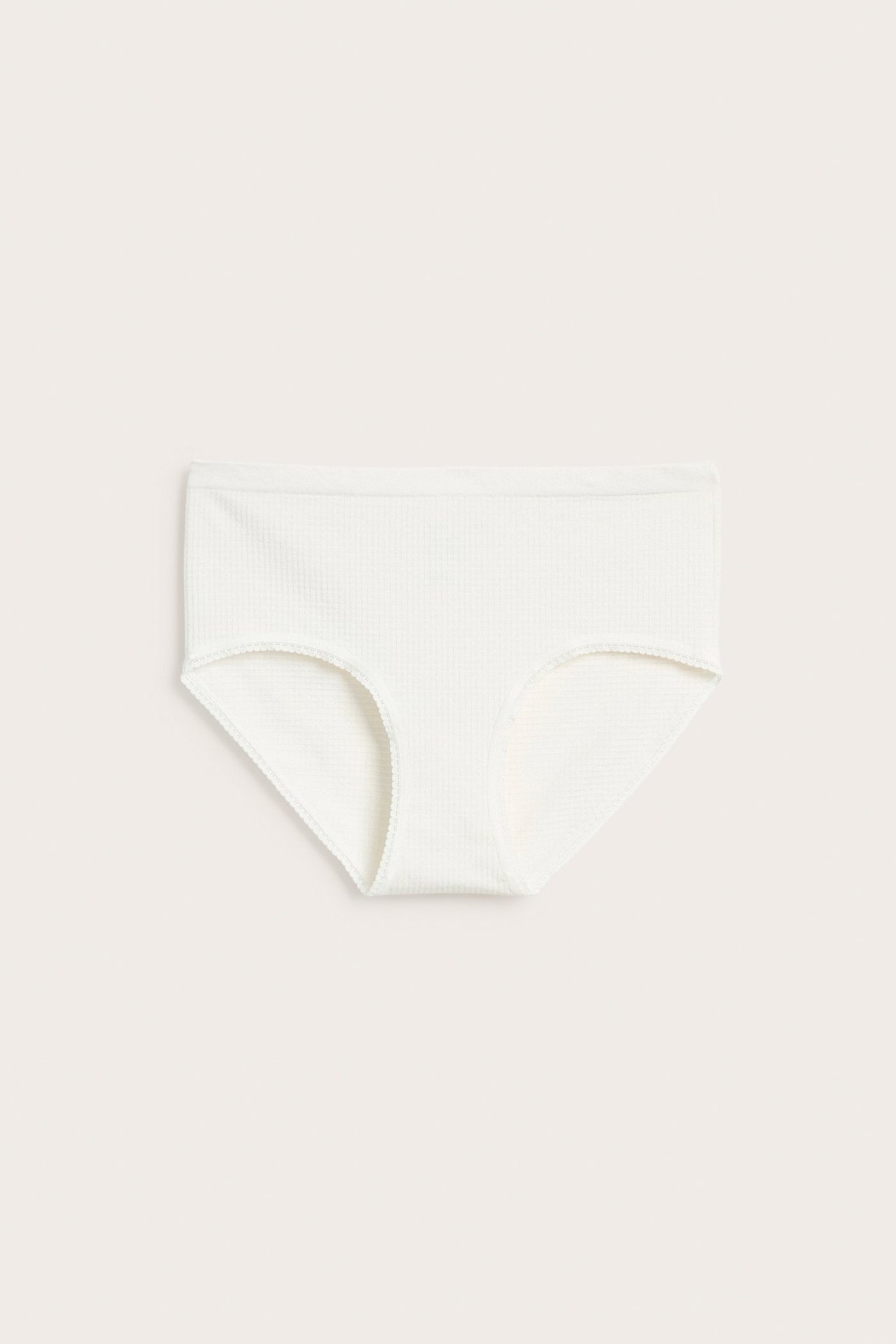 Frontvisning av hvit sømløs hipster-truse for dame med vaffelstruktur og myk blondekant.