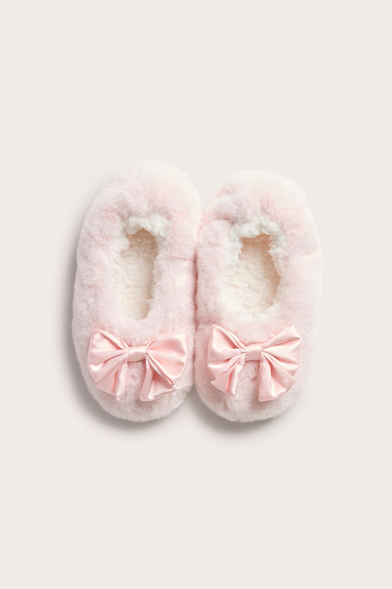 Widok z góry na parę jasnoróżowych kapci ze sztucznego futra z satynowymi kokardkami i puszystą podszewką.