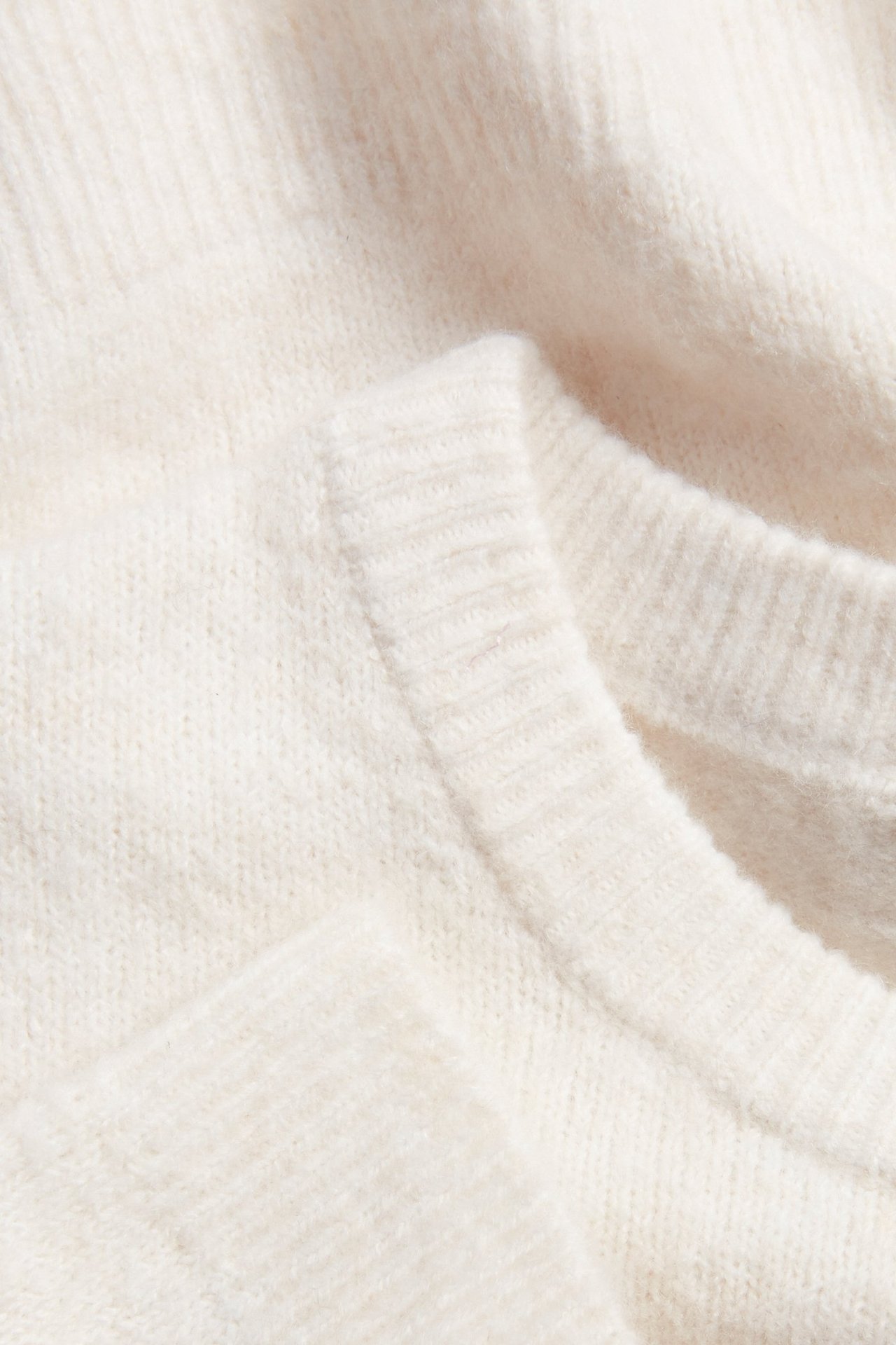Zbliżenie białego melanżowego swetra z delikatnej dzianiny z prążkowanym dekoltem.