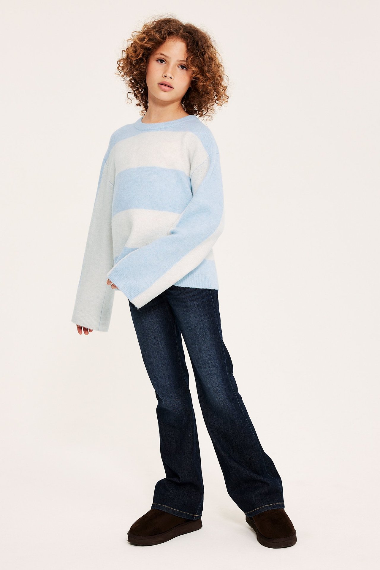 Frontvy: Kid i ljusblå och vitrandig stickad tröja, mörkblå jeans och bruna skor.
