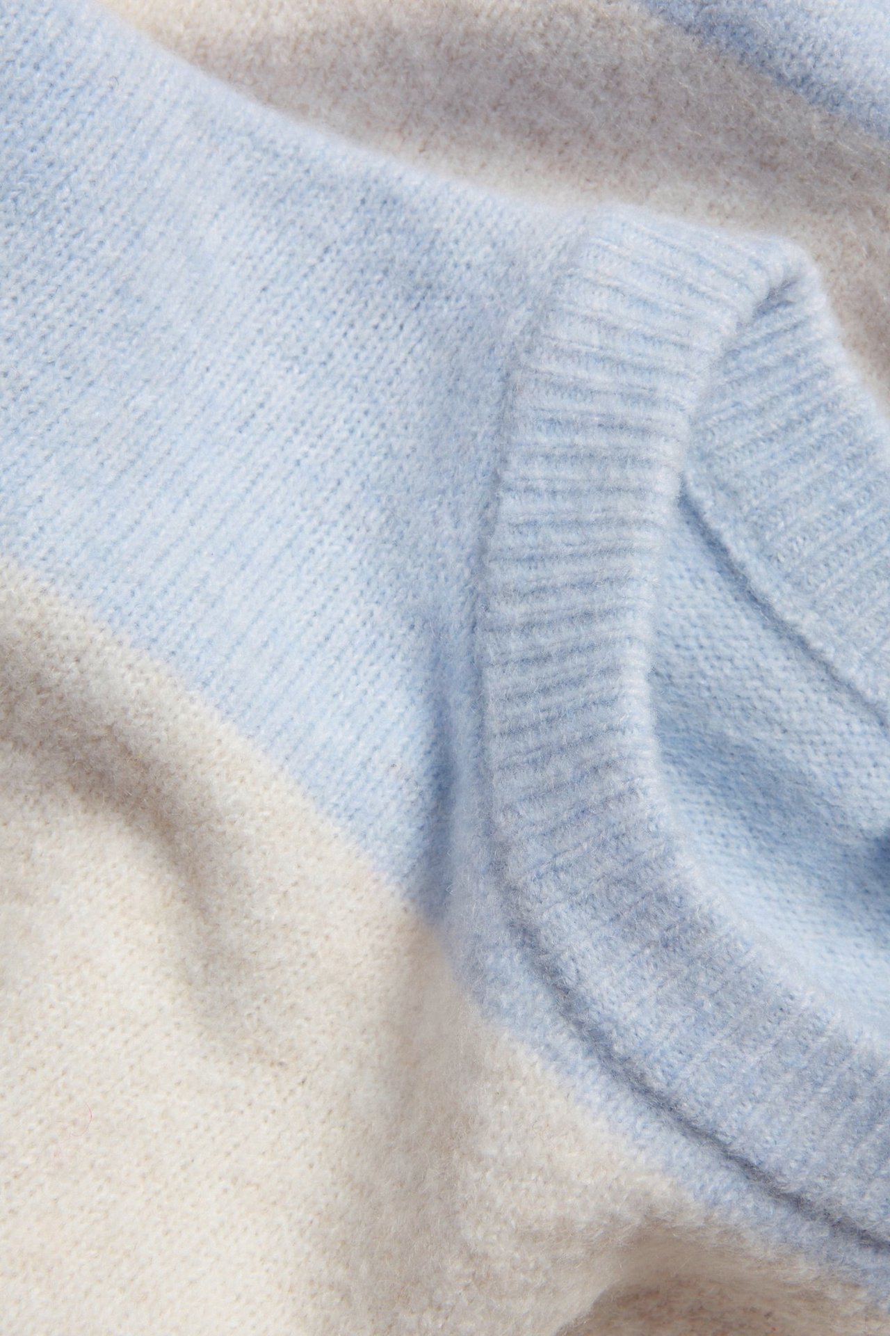 Zbliżenie na miękki, drobno tkany sweter w paski z jasnoniebieskimi, beżowymi i kremowymi paskami.