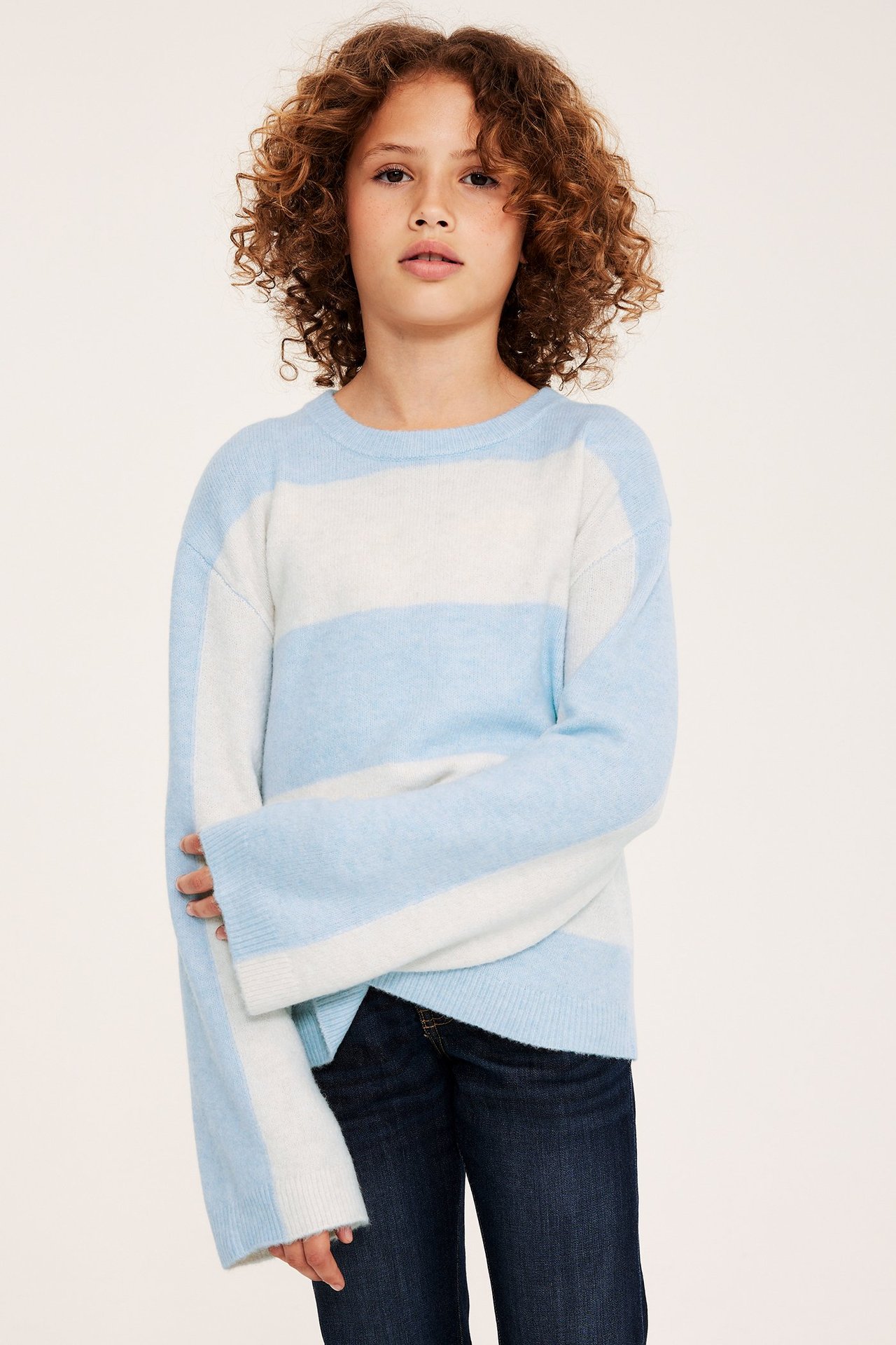 Frontvy av ett barn i en blåvit randig finstickad tröja och mörkblå jeans.