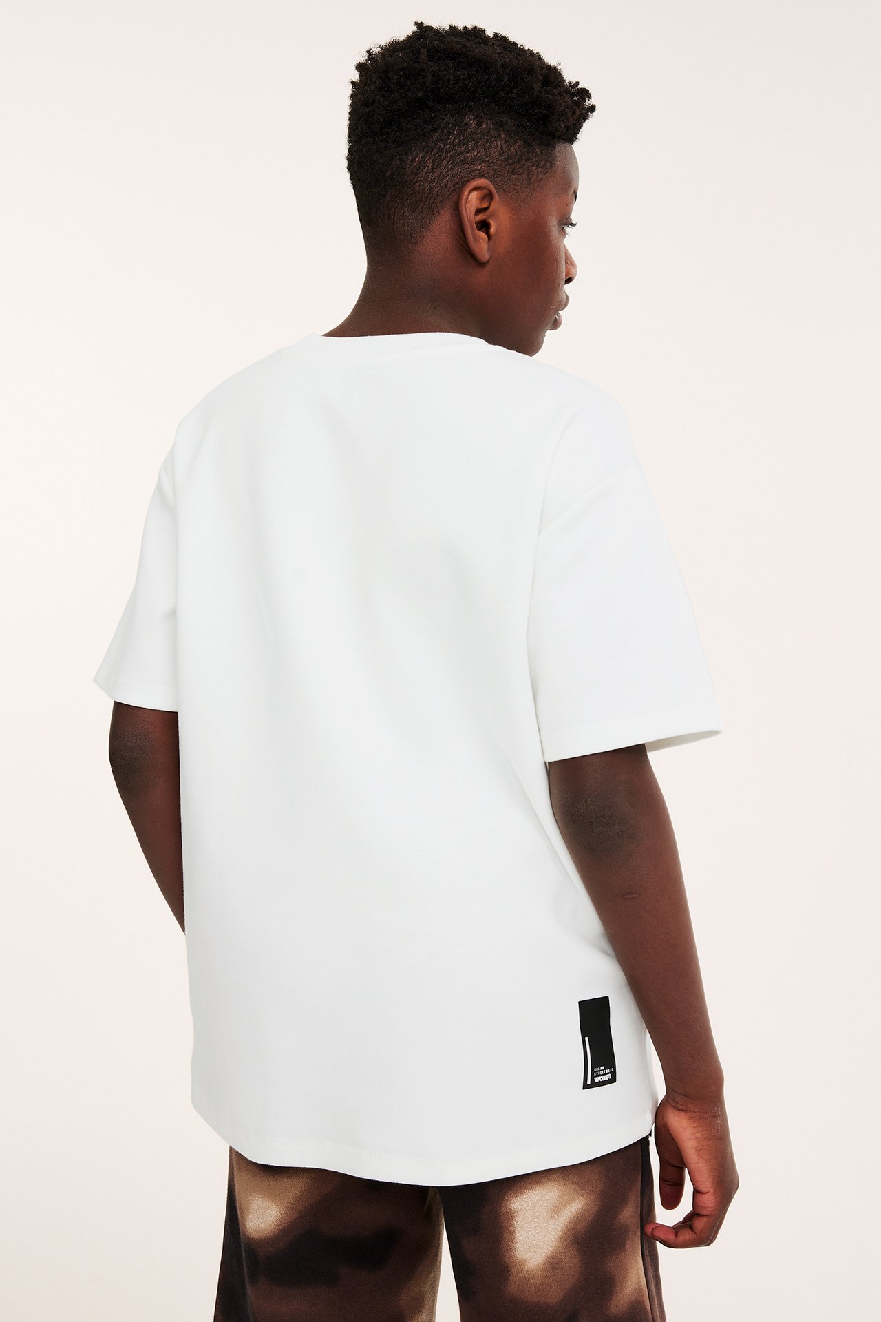 Bakifrån: ett barn i en offwhite oversized t-shirt och bruna tie-dye shorts.