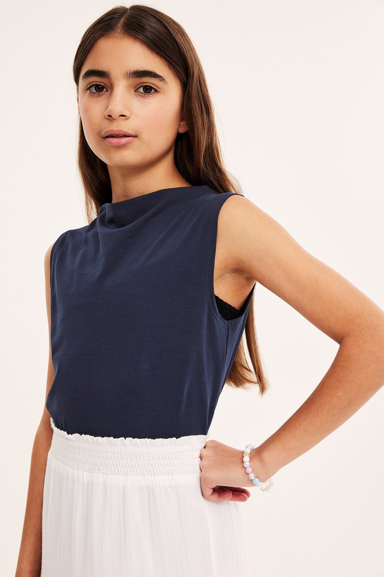 Widok z przodu: Dziecko nosi granatowy top bez rękawów z dekoltem w łódkę, białą spódnicę i bransoletkę.