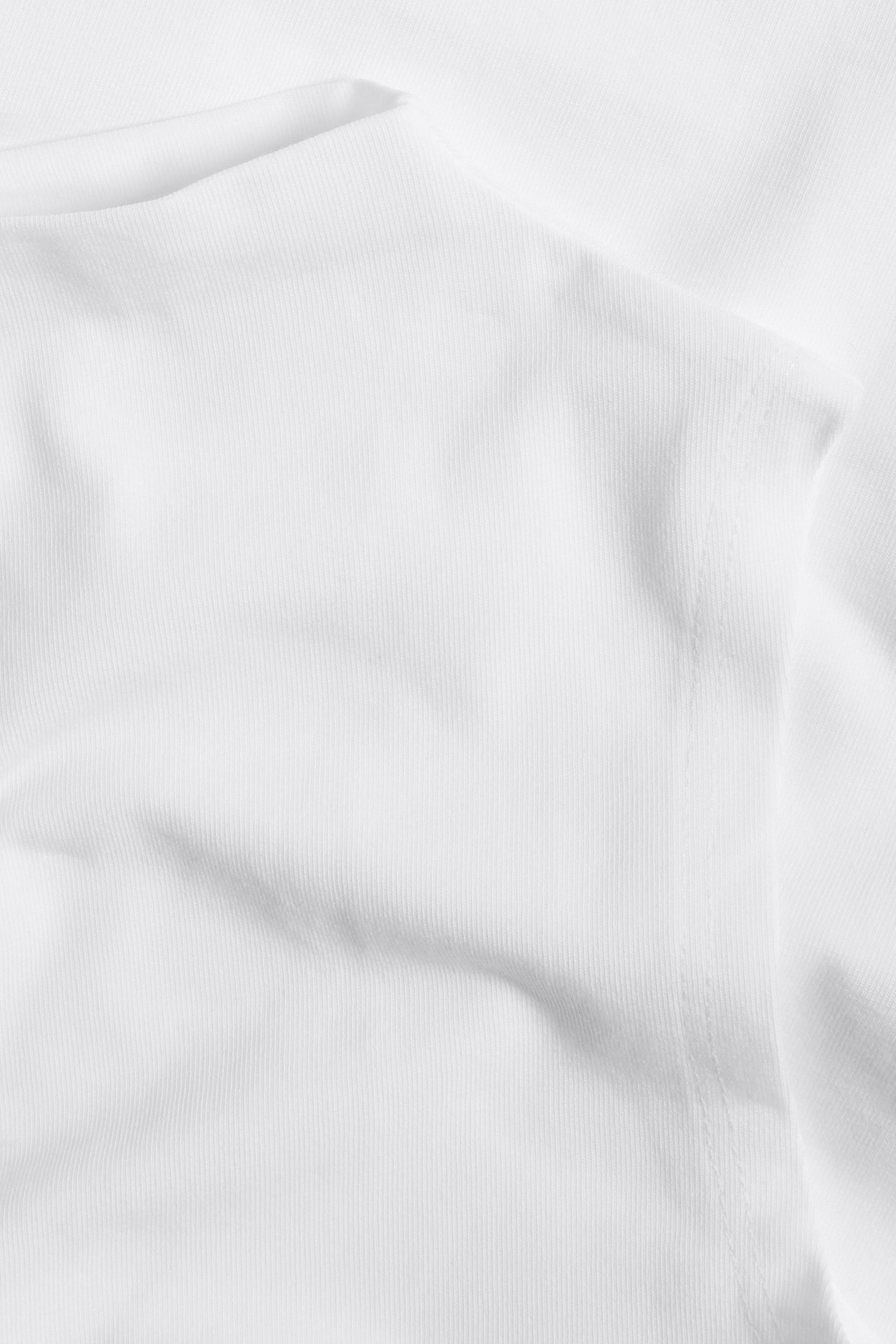 Zbliżenie białego, jednolitego, prążkowanego topu z mieszanki bawełny z fałdami.