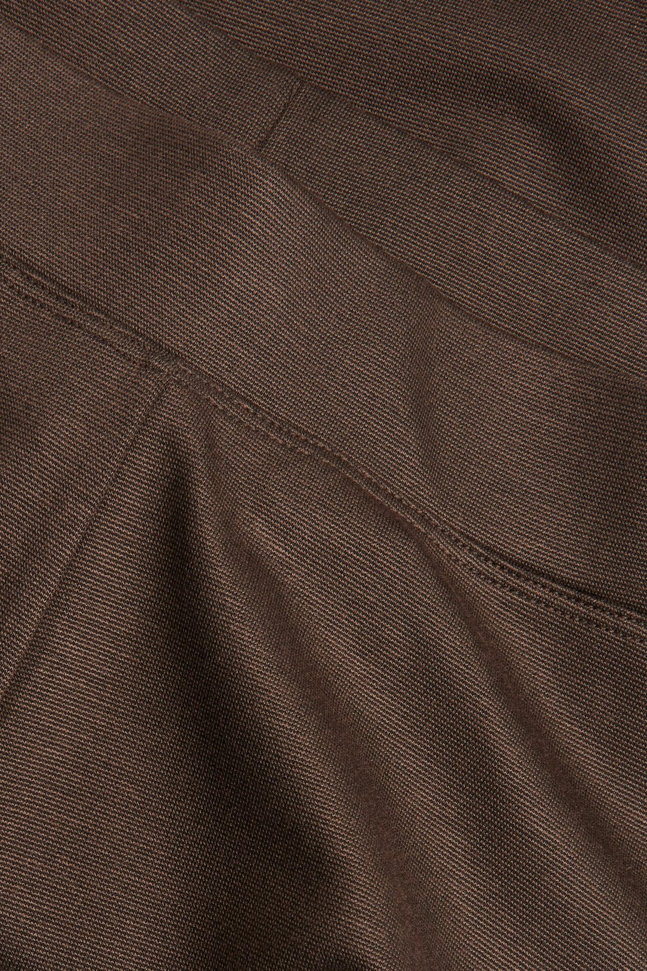 Zbliżenie na ciemnobrązowe dżersejowe spodnie bootcut, ukazujące teksturę materiału i widoczne szwy.