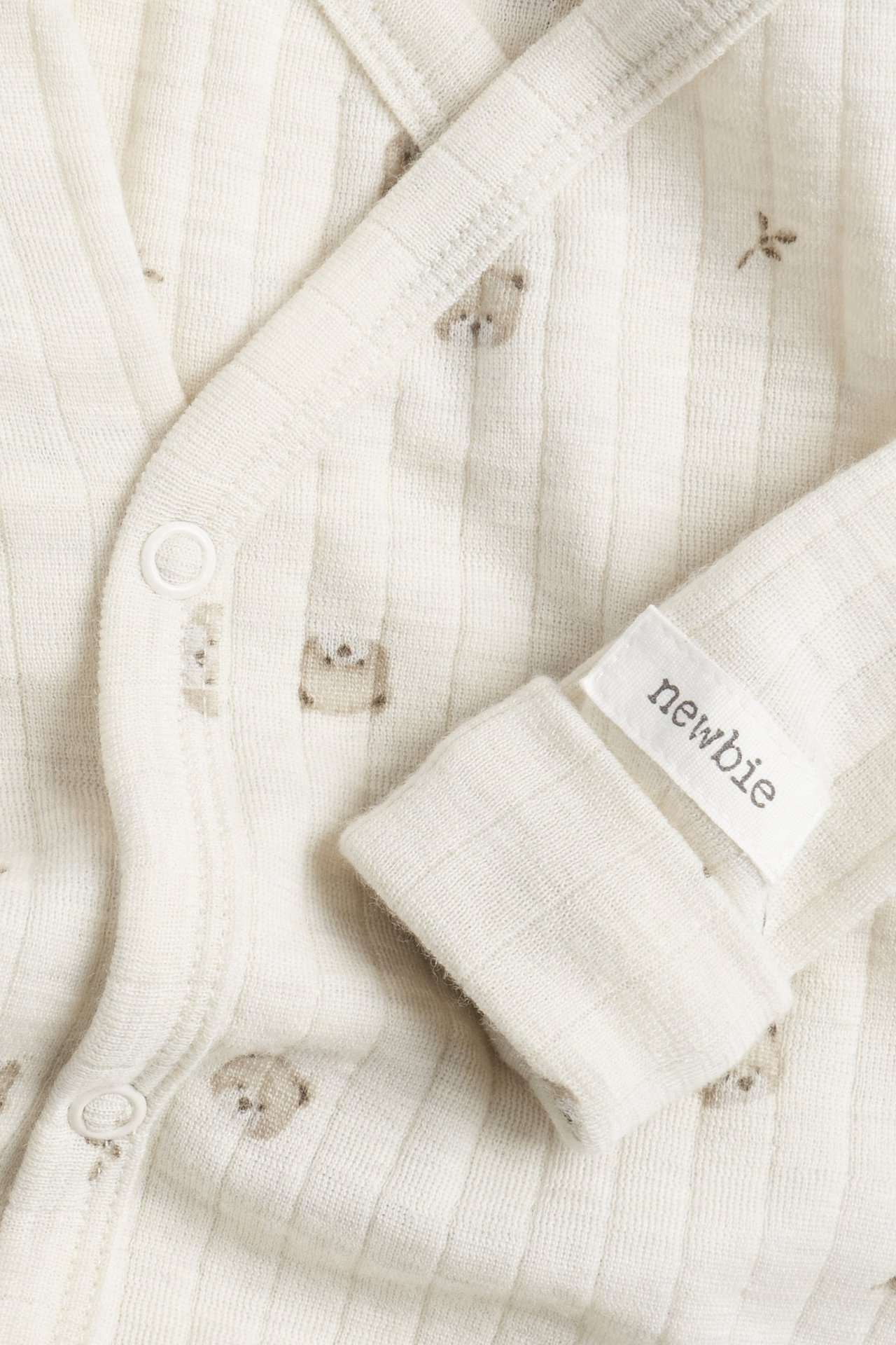 Närbild: Beige melange ribbad merinoull-body för baby med djurmönster, omlottstil och tryckknappar.