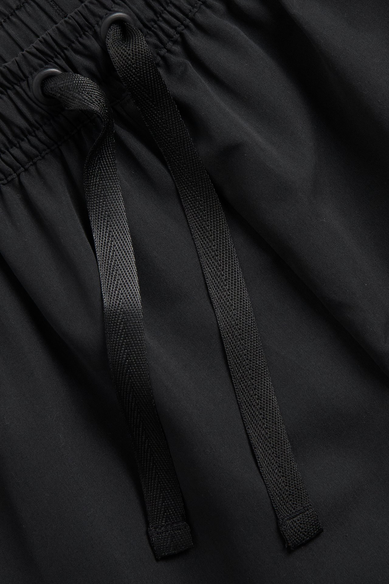 Nærbilde av svarte vevde polyester badeshorts med snøring i midjen.