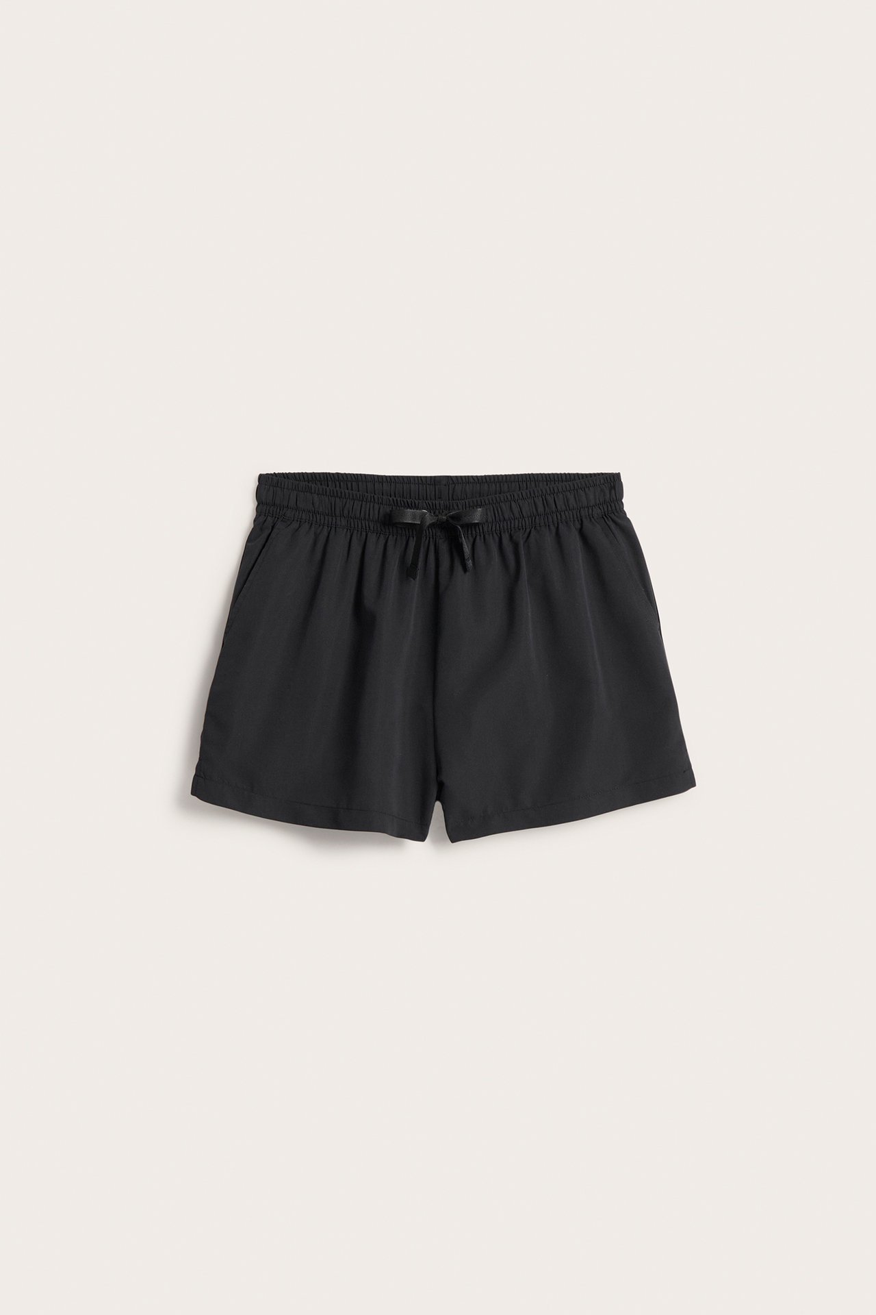 Frontvisning av svarte vevde badeshorts med høyt liv, elastisk snøring i midjen og lommer.