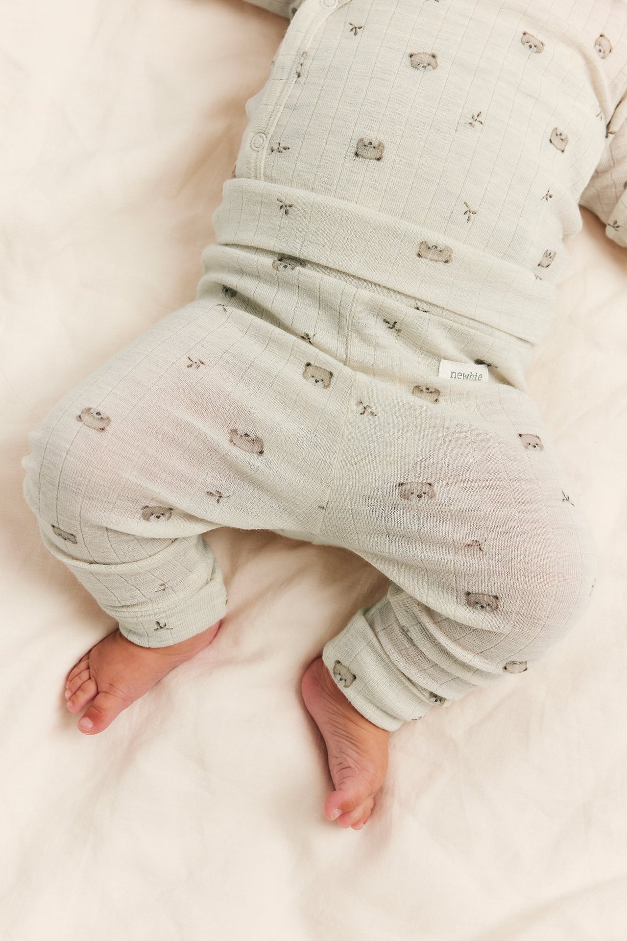 Lähikuva vauvasta vaaleanvihreässä ribbipyjamassa karhupainatuksella, neppareilla ja "newbie"-etiketillä.