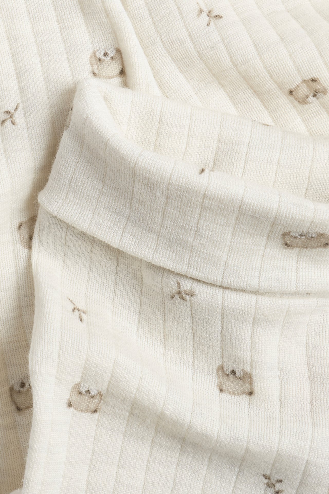 Närbild på vikt ljusbeige ribbad babyplagg med små bruna djurmönster.