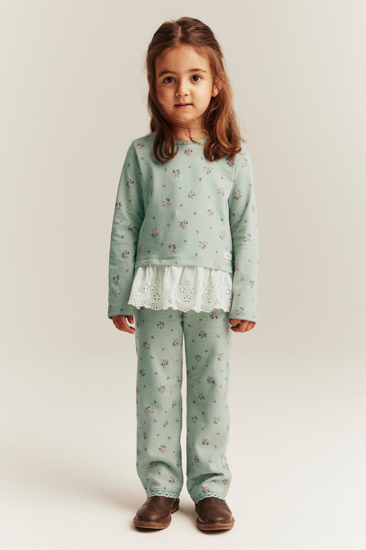 Widok z przodu dziecka w zielonych kwiecistych rozszerzanych legginsach z dżerseju i pasującej bluzce z długim rękawem.
