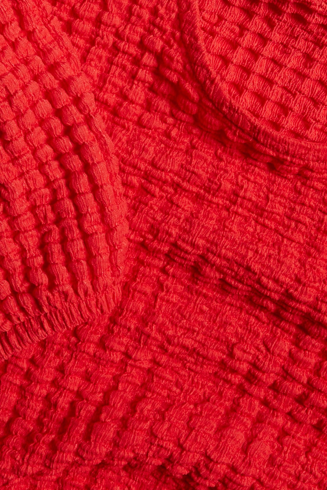 Zbliżenie na czerwoną, strukturalną tkaninę bluzki z bufiastymi rękawami.