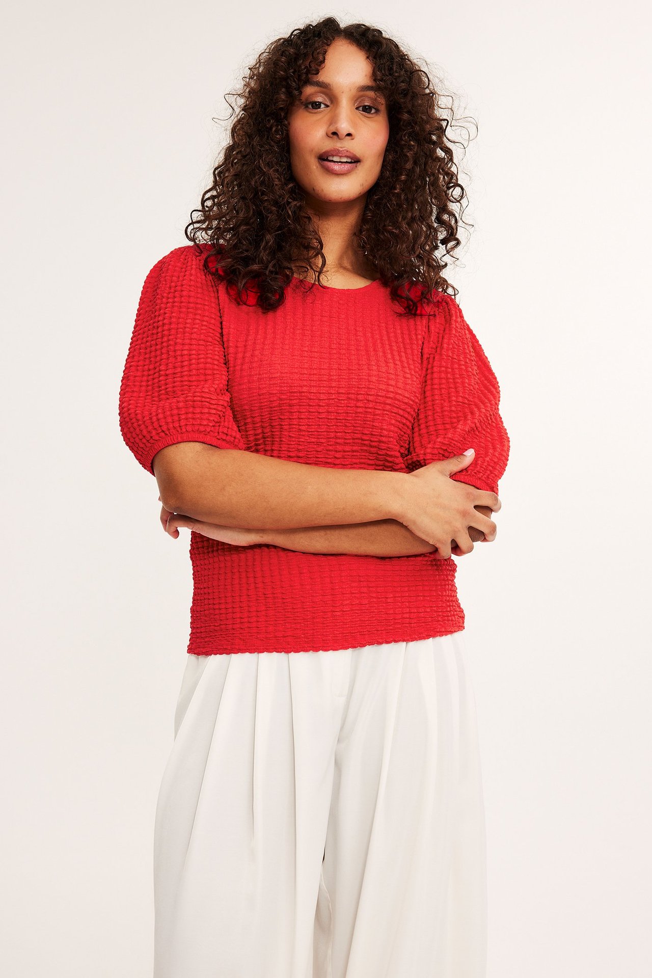 Widok z przodu kobiety w czerwonym topie z bufiastymi rękawami i białych szerokich spodniach.