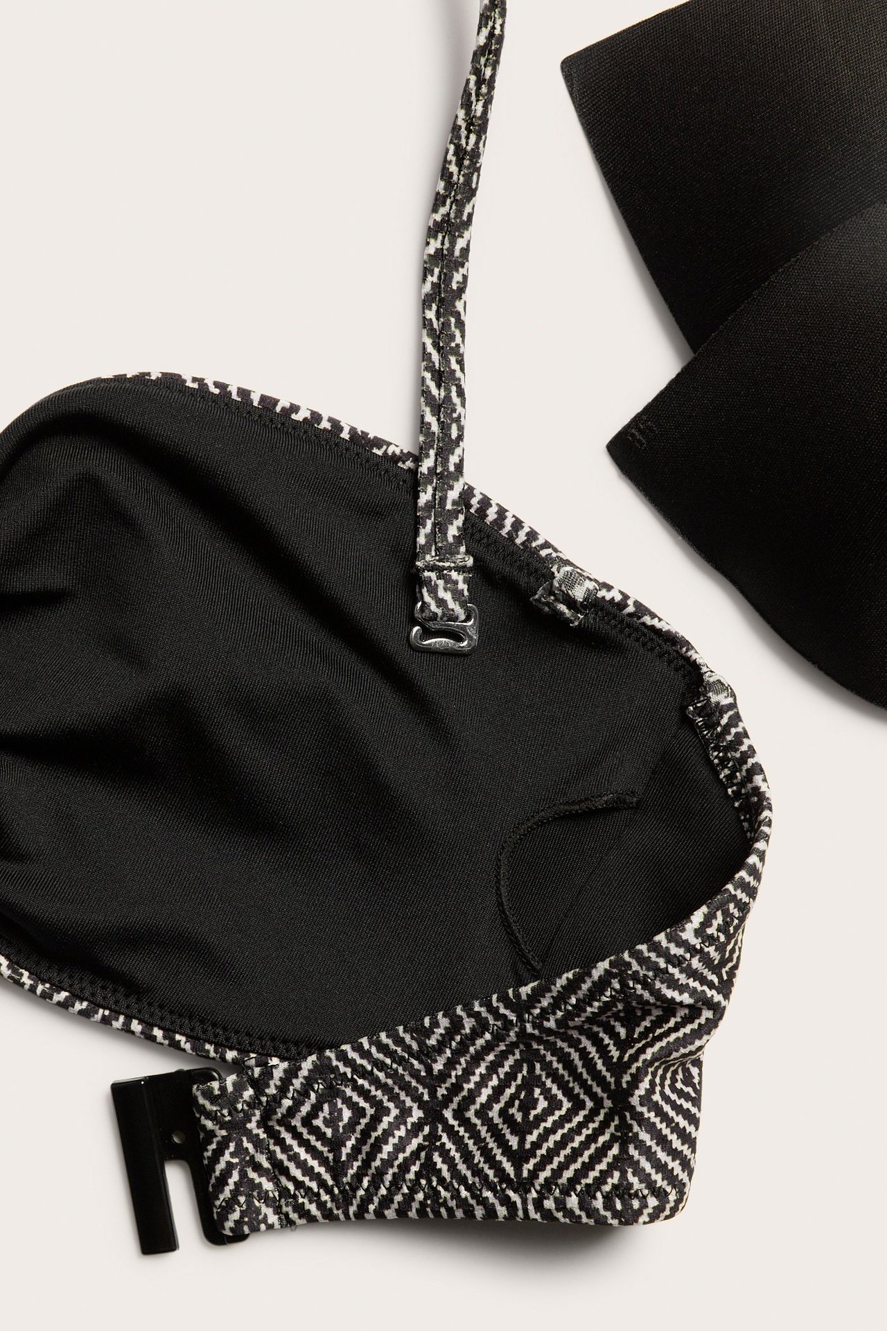 Zbliżenie na czarno-biały wzorzysty top bikini bandeau z odpinanym paskiem na szyję i zapięciem z tyłu.