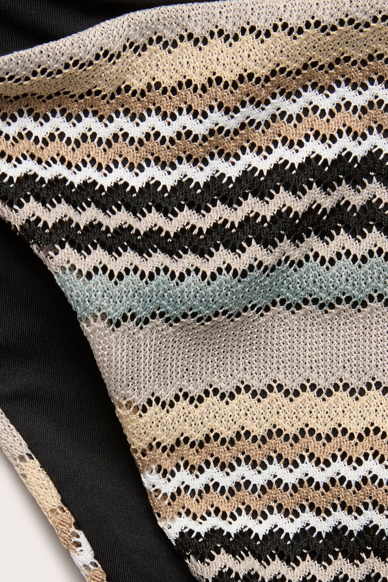 Zbliżenie na wielokolorowy, dziergany dół bikini z beżowym, białym, czarnym i niebieskim wzorem zygzakowym.