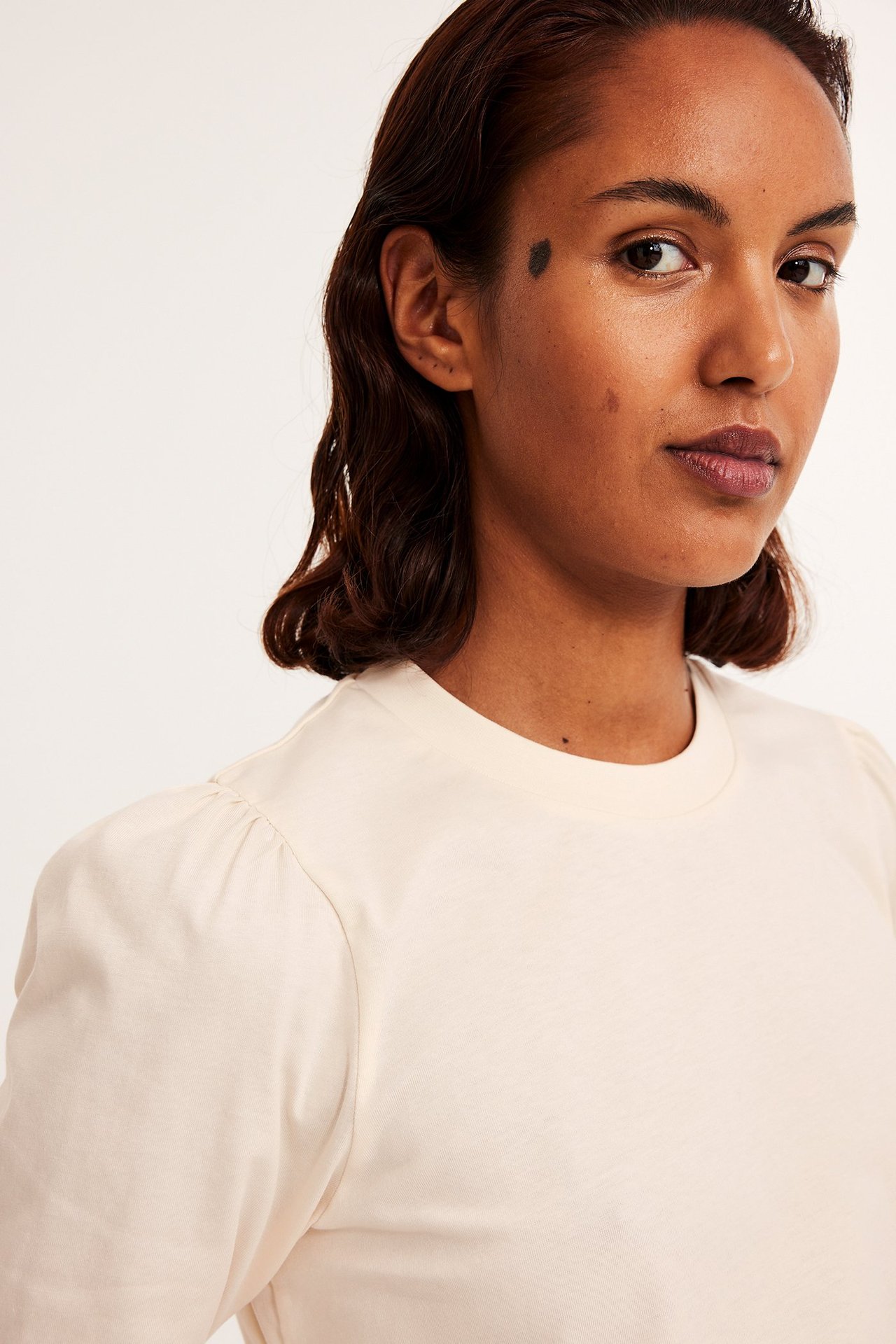 Nærbilde forfra av en kvinne i offwhite bomullstopp med korte puffermer.