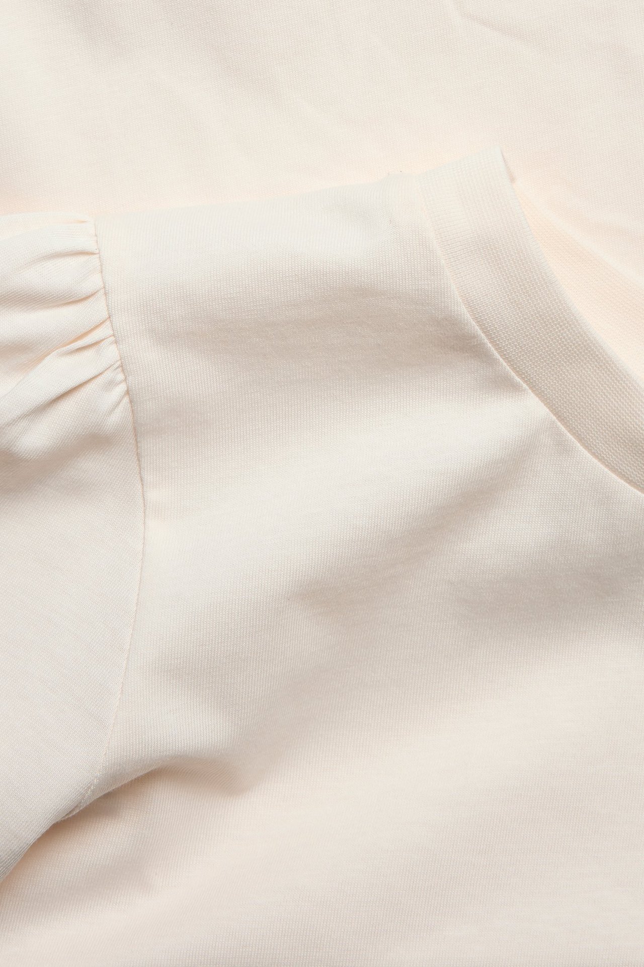 Zbliżenie na kremowy bawełniany top z marszczonymi bufiastymi rękawami i prążkowanym okrągłym dekoltem.