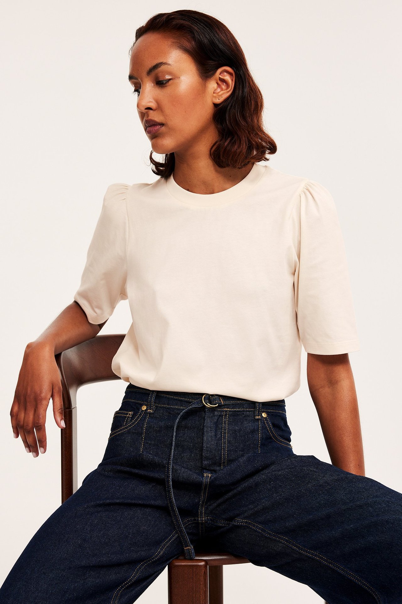 Forfra: kvinne i offwhite topp med puffermer og mørkeblå jeans.
