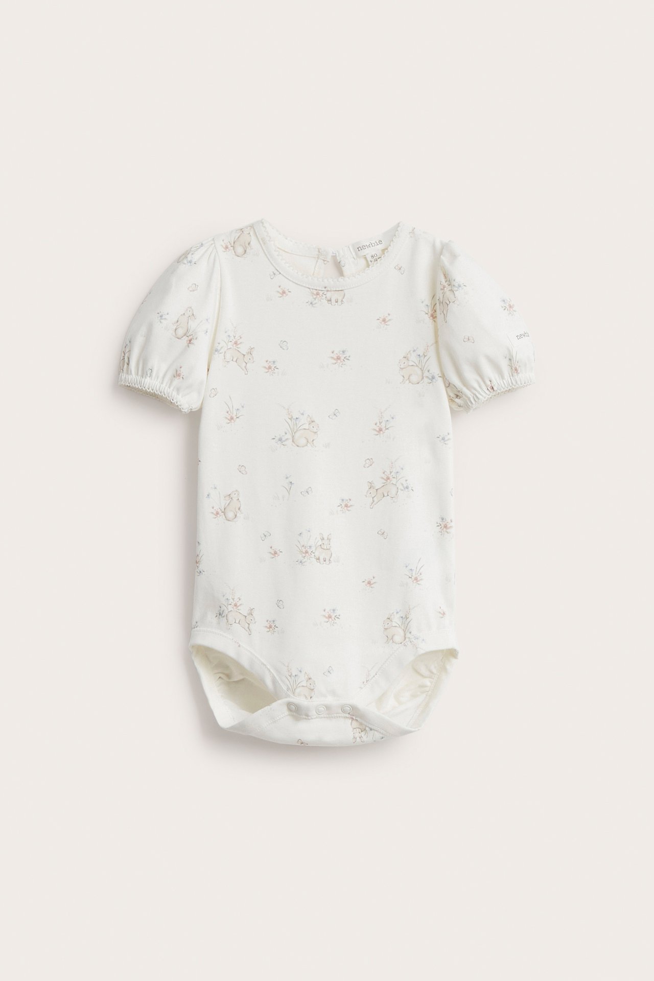 Frontvisning: Off-white babybody med kanin- og blomstermønster, korte puffermer, trykknapper.