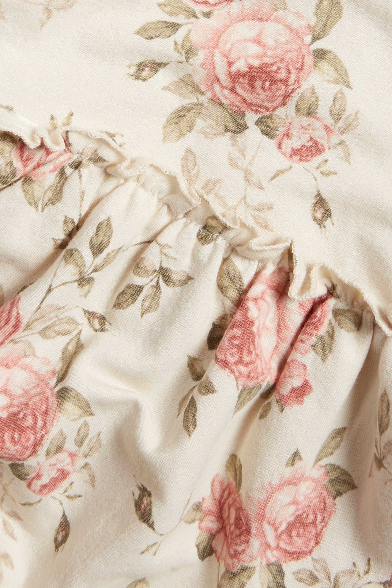 Zbliżenie na jasnobeżowy materiał sukienki z dżerseju z różanym wzorem i falbanką.