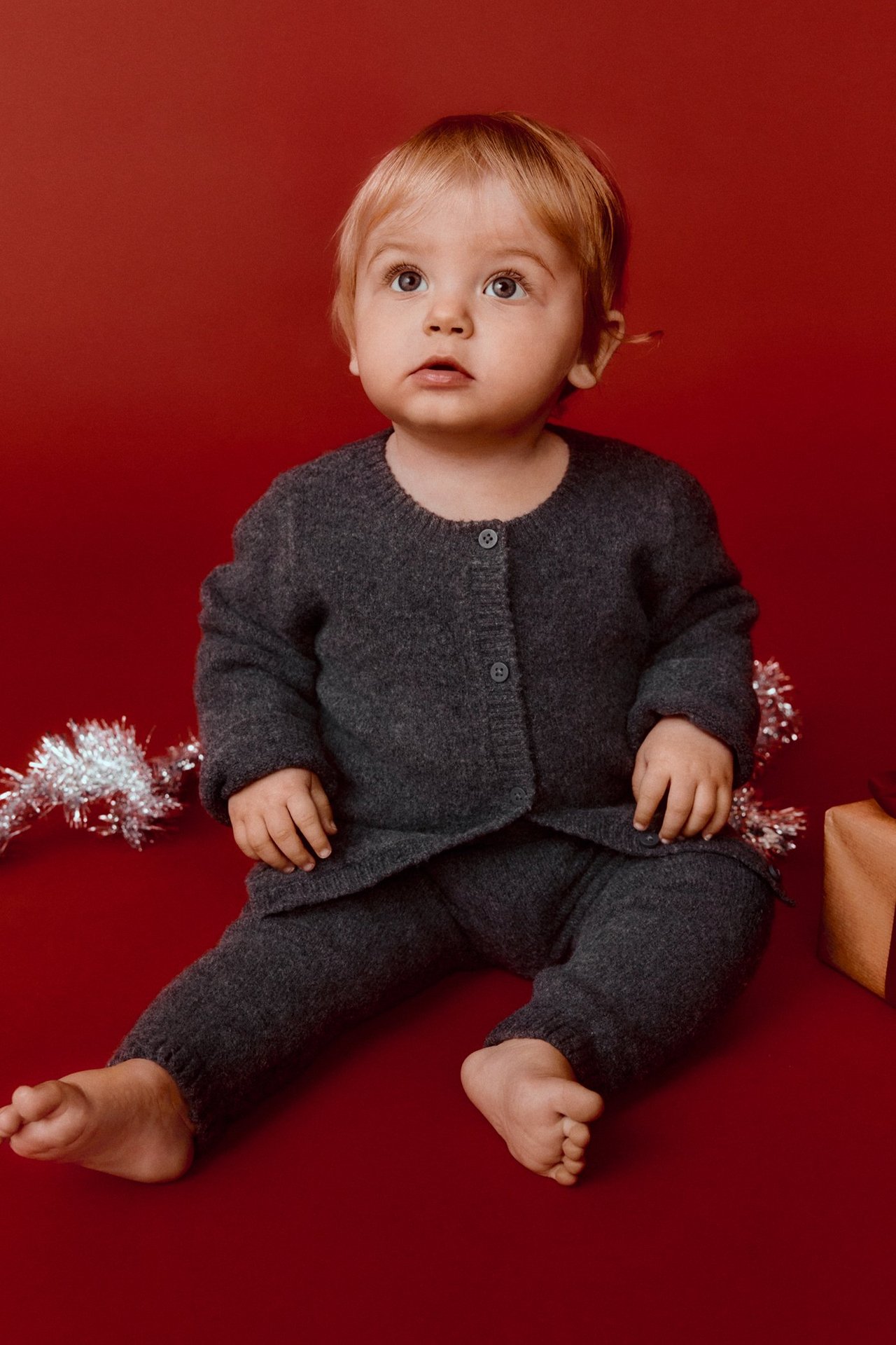 Vauva edestä, yllään tummanharmaa meleerattu neuletakki napeilla ja yhteensopivat neulehousut.