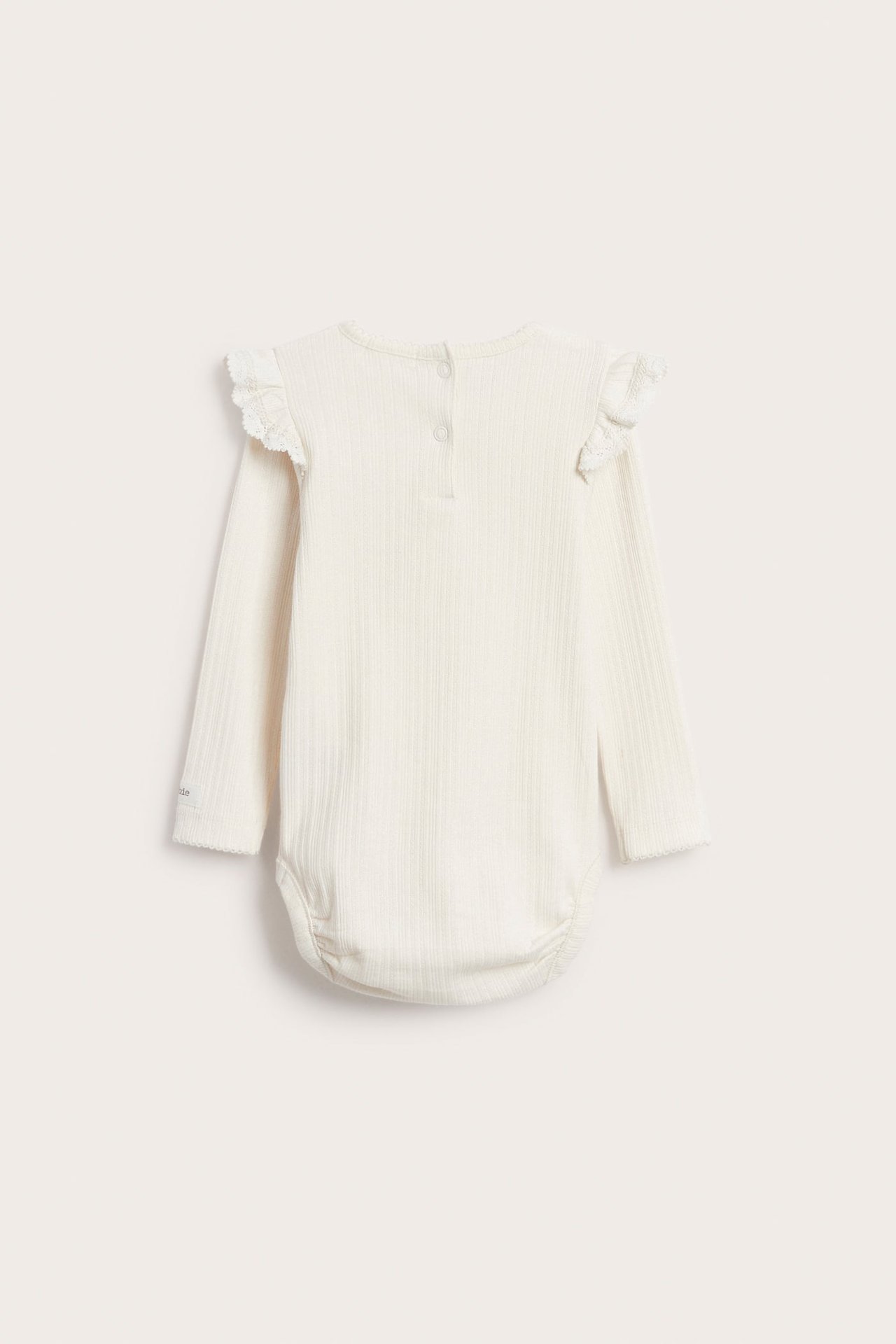 Ryggvy av en offwhite ribbad långärmad babybody med volanger, spets och tryckknappar i ryggen.