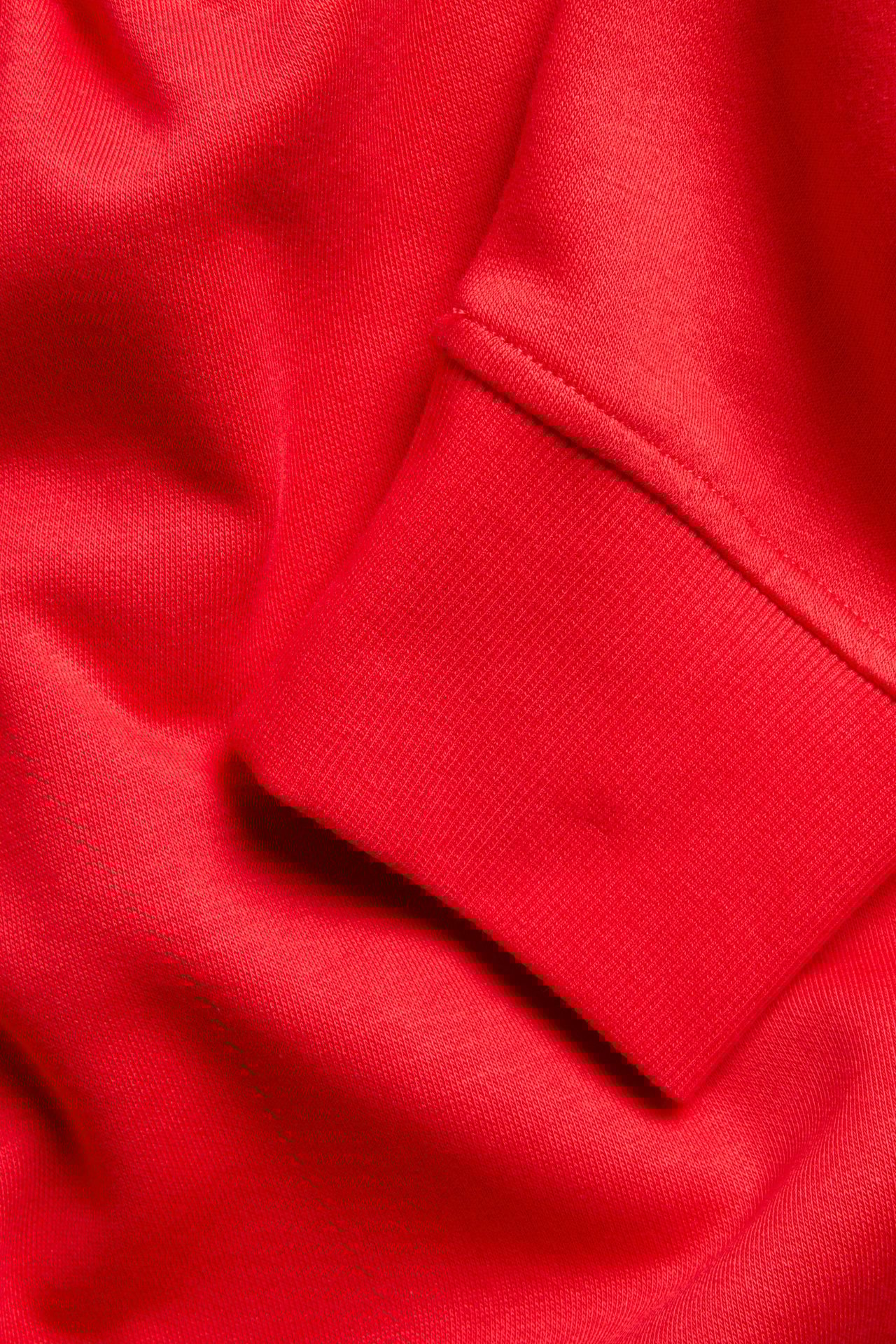 Zbliżenie czerwonego rękawa bluzy z mieszanki bawełny z prążkowanym mankietem.