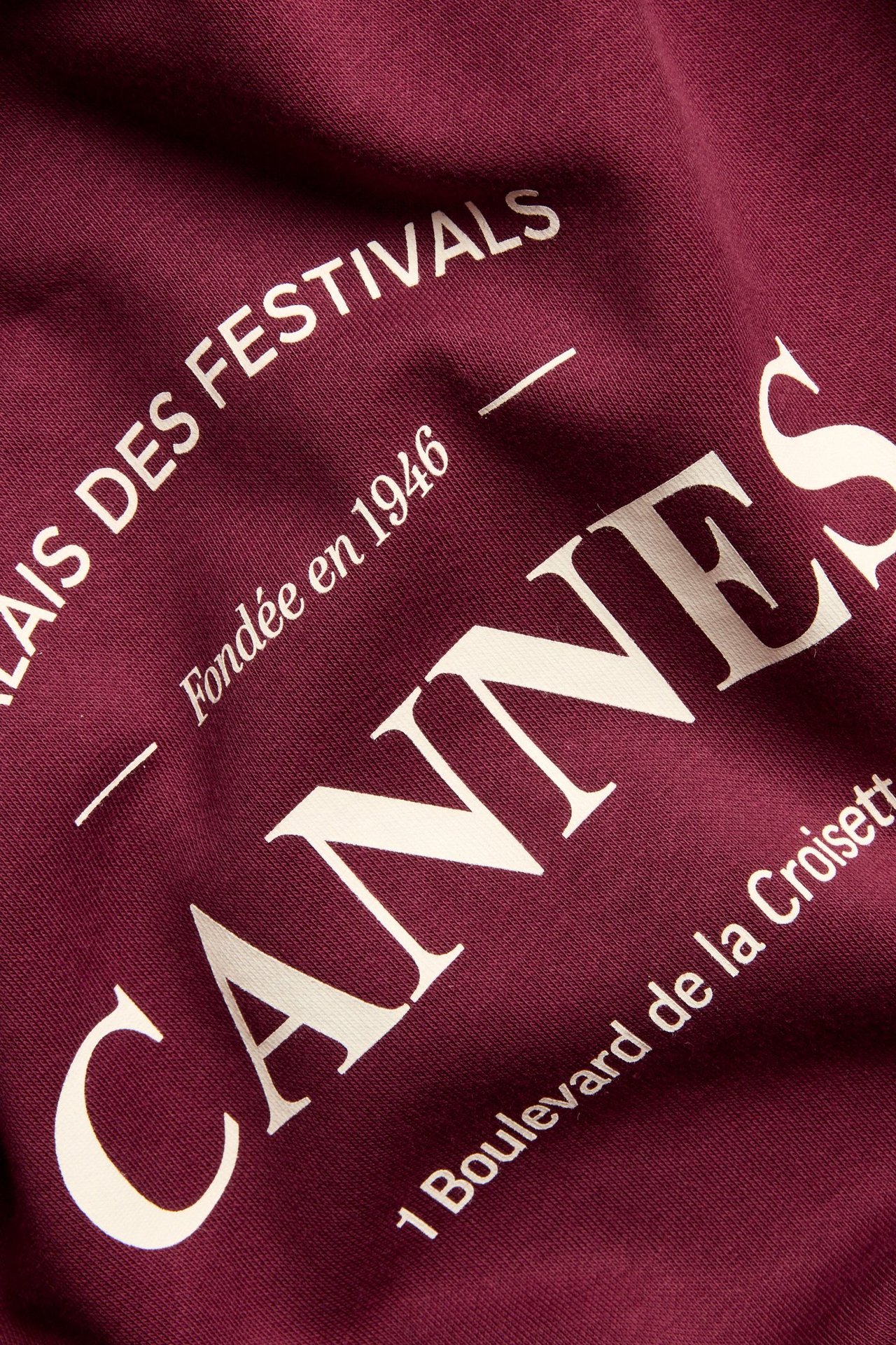 Zbliżenie na bordową bluzę z mieszanki bawełny z białym nadrukiem 'Cannes' z przodu.