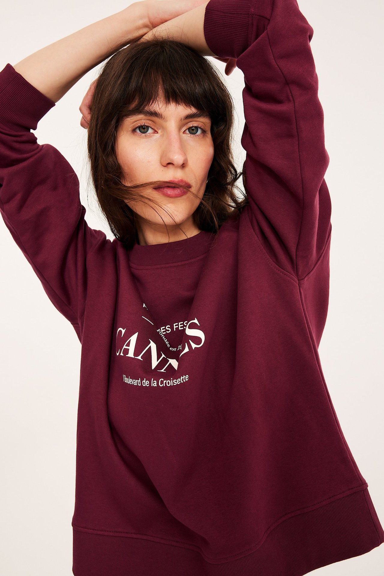 Nærbilde forfra av en kvinne i vinrød sweatshirt med hvitt "Cannes"-trykk.