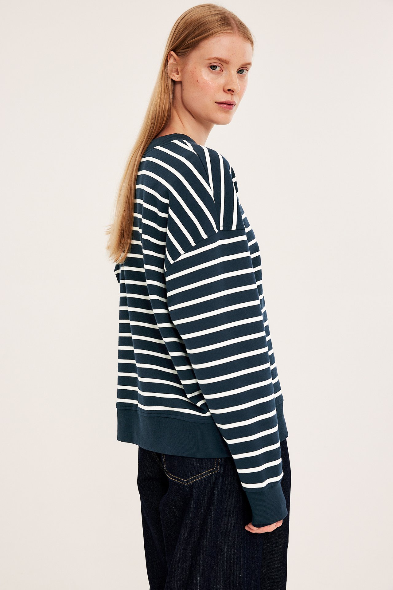 Sidovy av en kvinna i en mörkblå och vitrandig sweatshirt och mörkblå jeans.