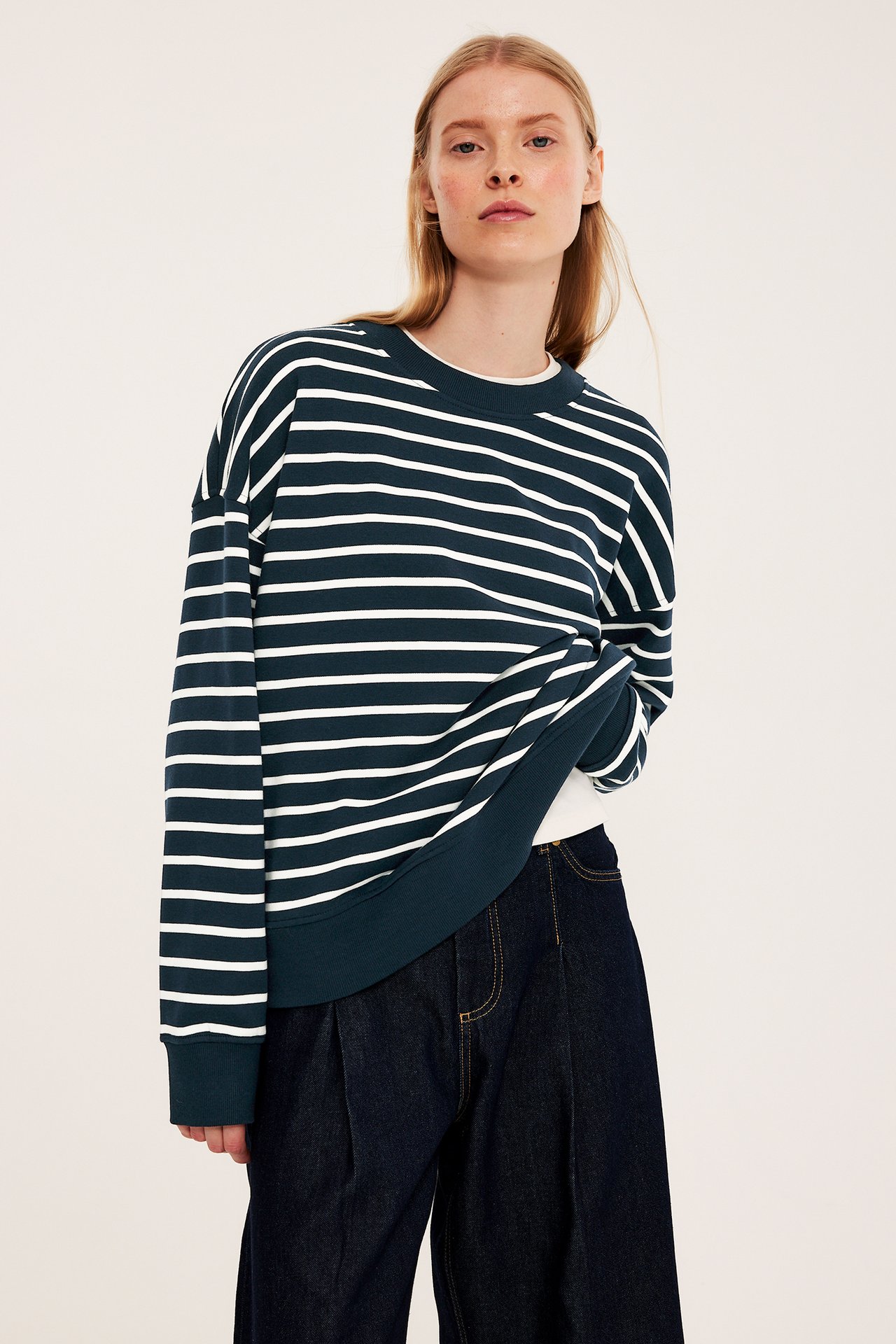 Framifrån: kvinna i mörkblå- och vitrandig sweatshirt, vit t-shirt och mörkblå vida jeans.