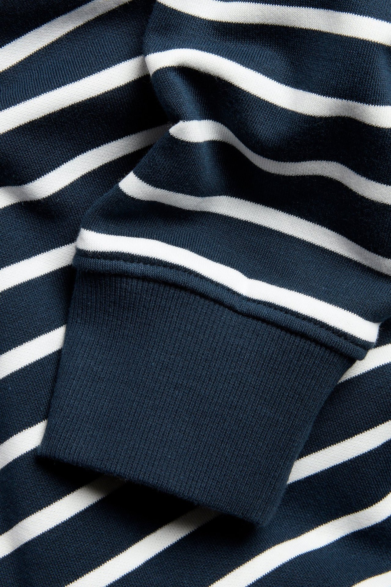 Zbliżenie na ciemnoniebiesko-biały, pasiasty rękaw bluzy z prążkowanym mankietem.