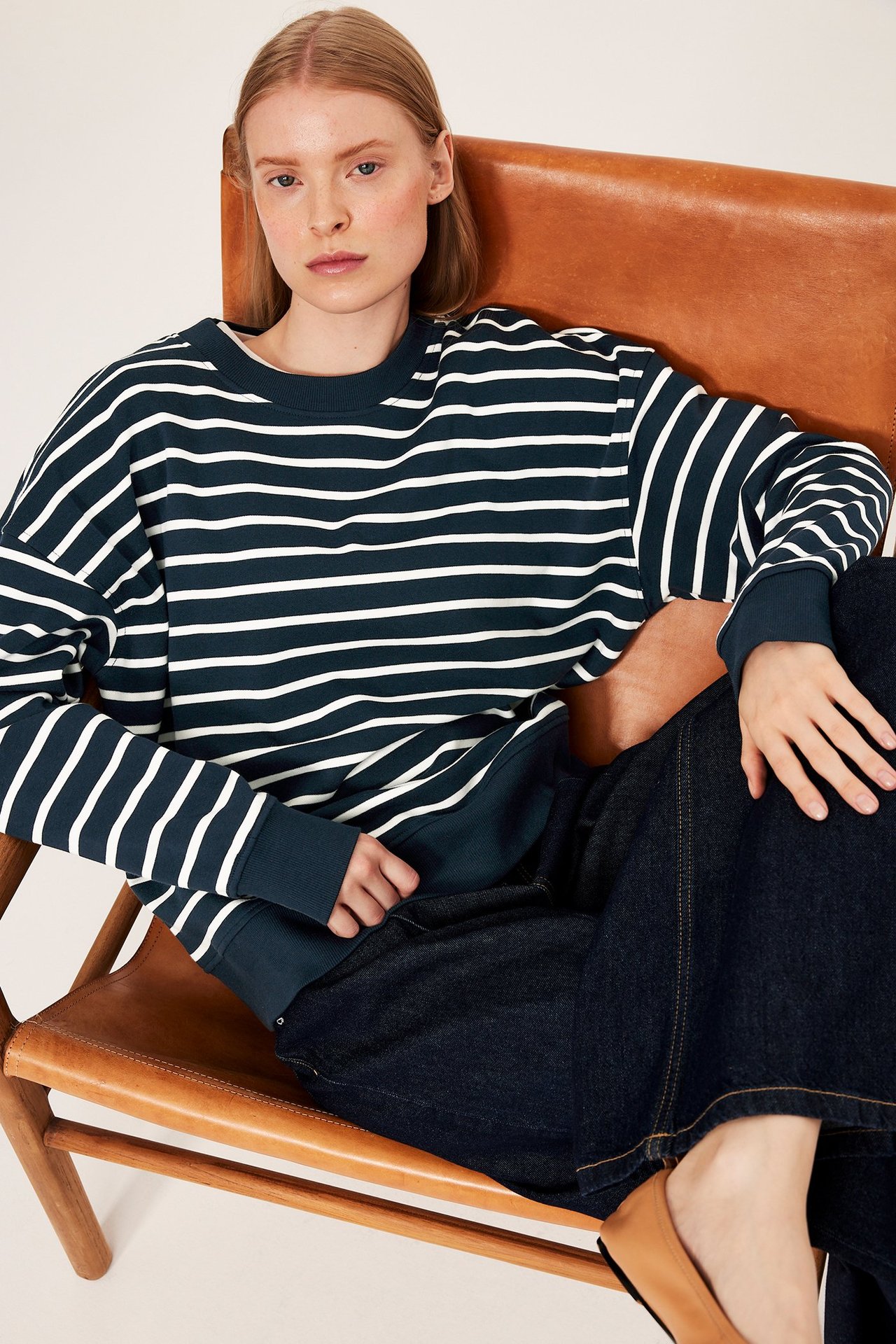Forfra: kvinne i mørkeblå stripet sweatshirt med avslappet passform, mørkeblå vide jeans og brune flate sko.