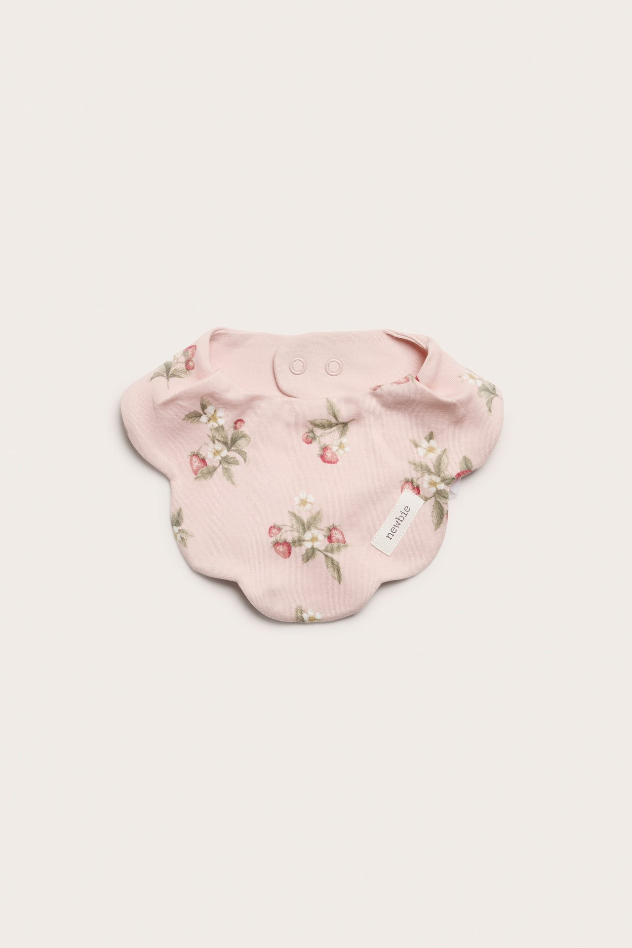 Ovanifrån: Ljusrosa babydregglis med jordgubbs- och blommönster, vågig kant och tryckknappar.