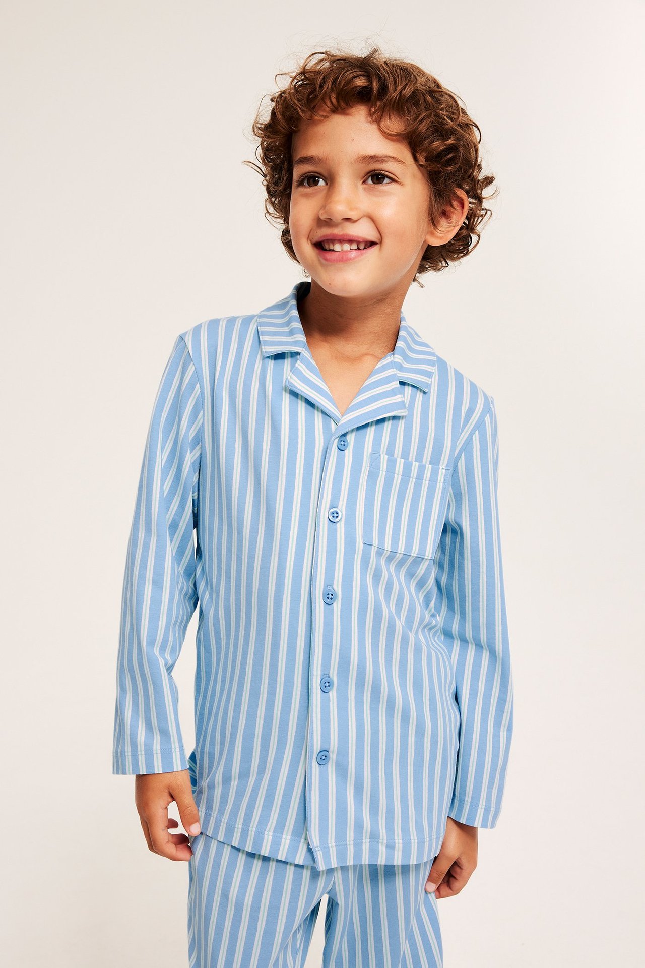 Edestäpäin, lapsi yllään vaaleansinivalkoraidallinen trikoopyjama nappikiinnitteisellä paidalla.