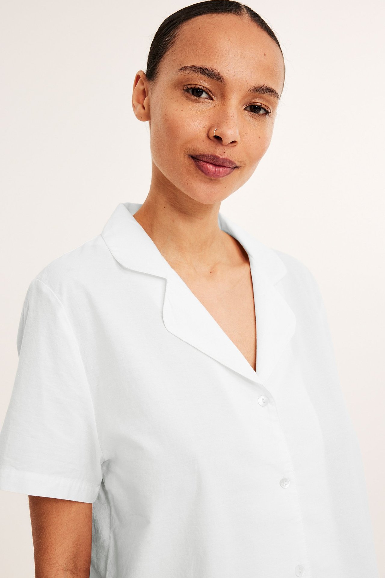 Lähikuva edestä: nainen yllään luonnonvalkoinen puuvillapyjamatoppi lyhyillä hihoilla ja kauluksella.