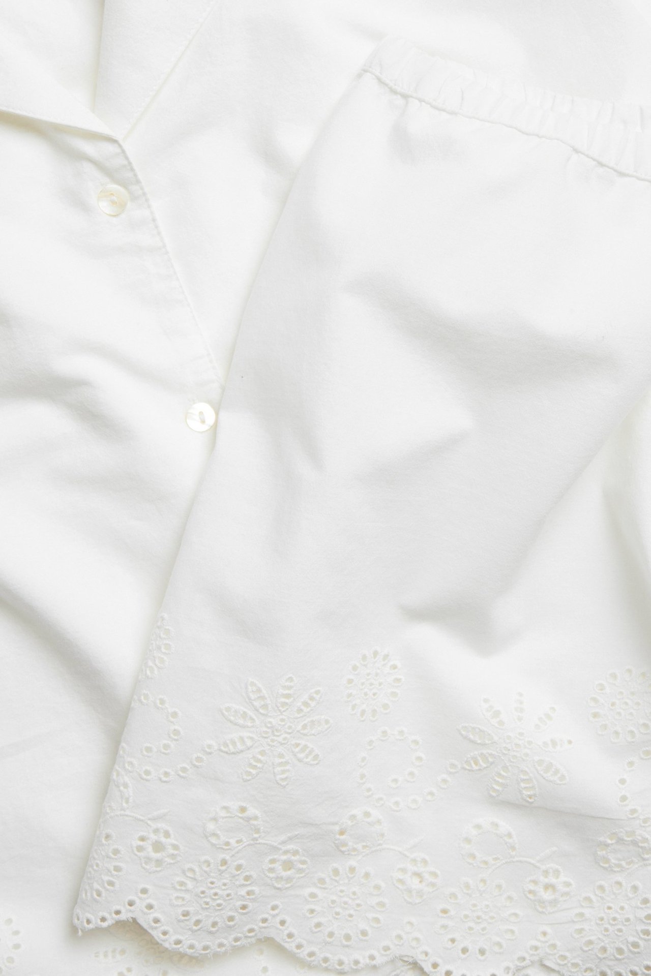 Zbliżenie na ecru bawełnianą piżamę z zapinaną górą i haftowanym obszyciem na spodniach.