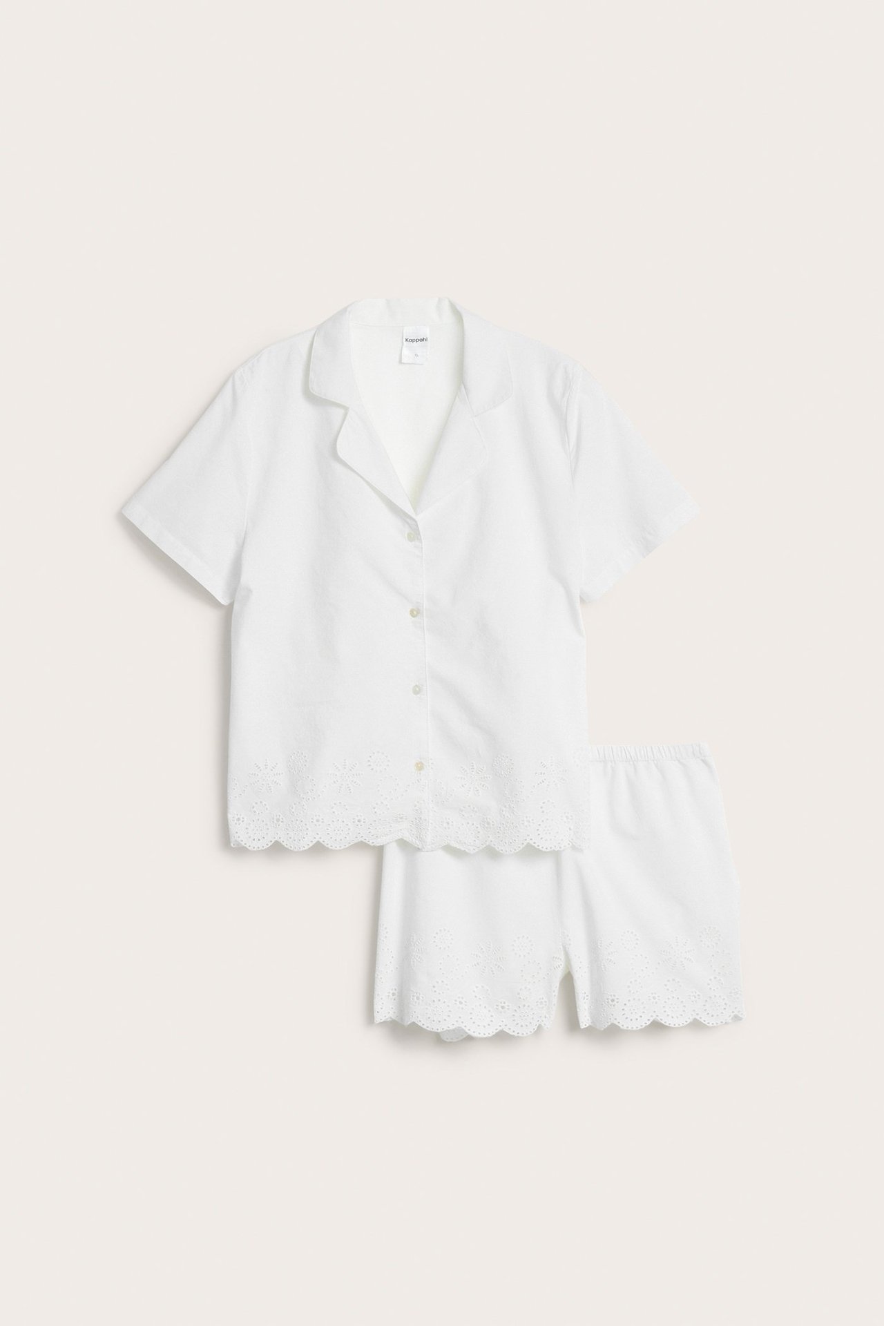 Edestä: Luonnonvalkoinen puuvillapyjama, lyhythihainen paita ja shortsit brodeeratuilla aaltoilevilla reunoilla.